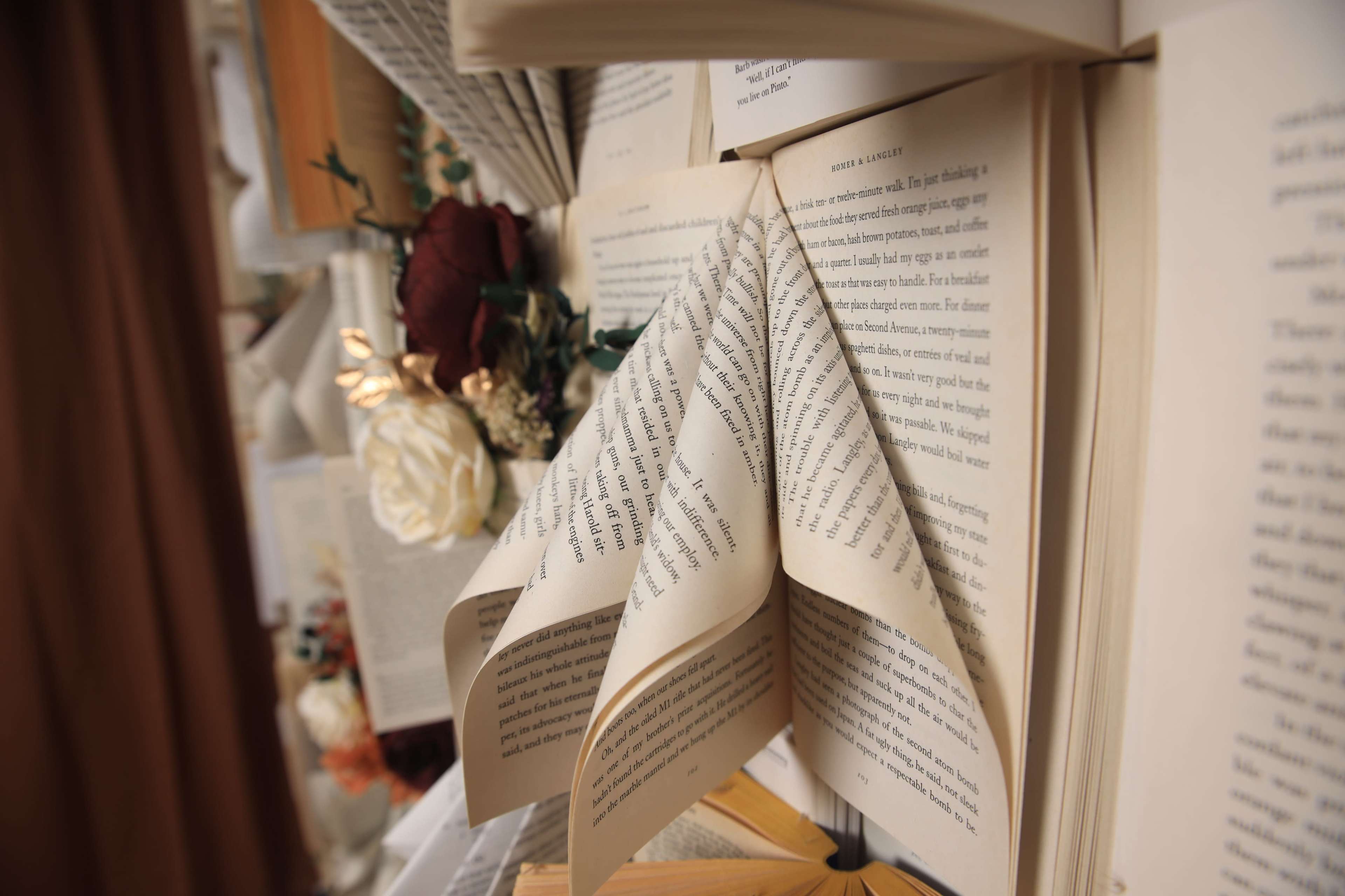 The image shows several open books displayed with turned pages, surrounded by flowers and decor.