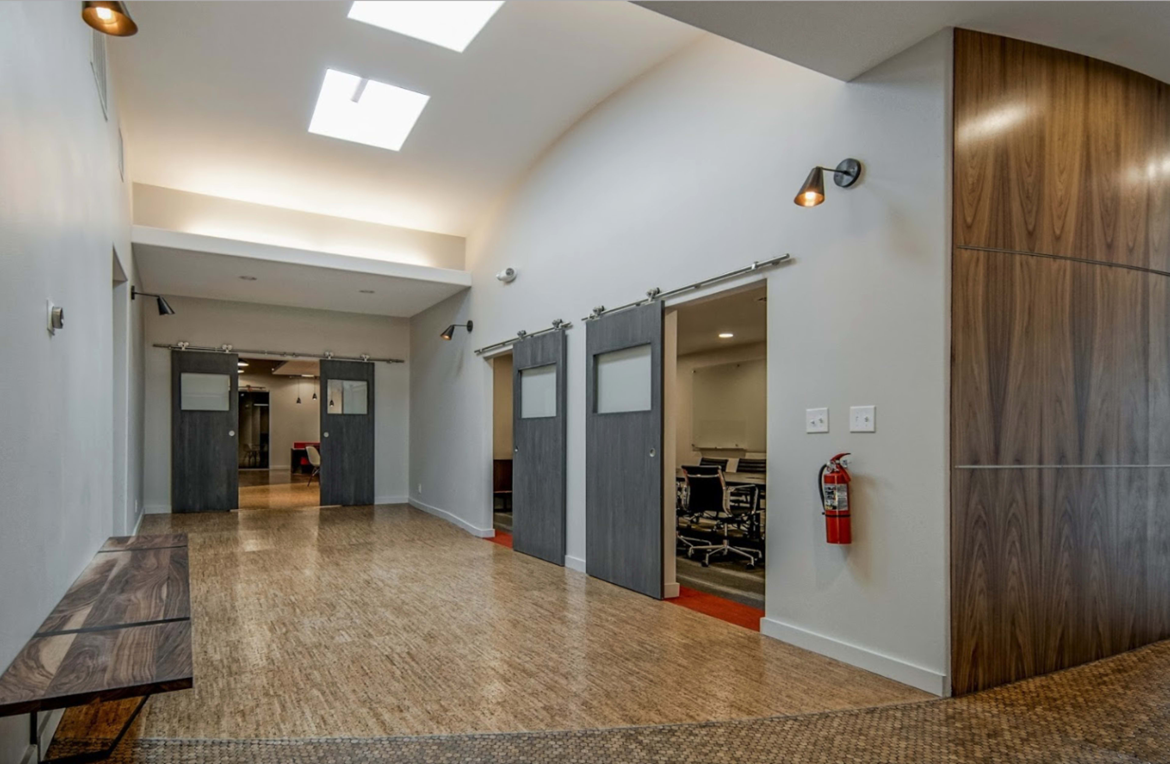 A modern hallway with sliding barn doors leading to meeting rooms and a wooden bench along one side.