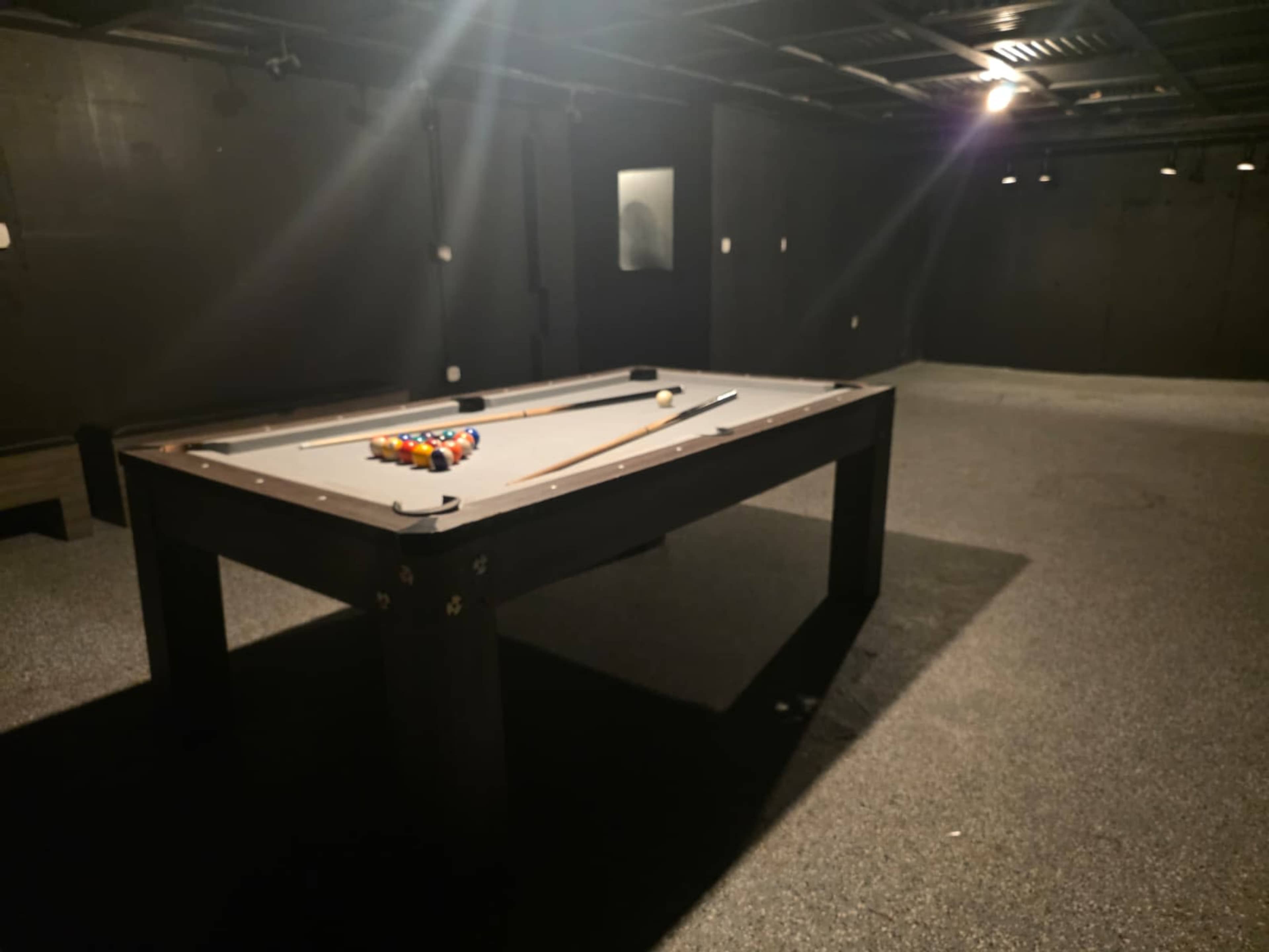 A pool table is positioned in a dimly lit room with dark walls and a carpeted floor.