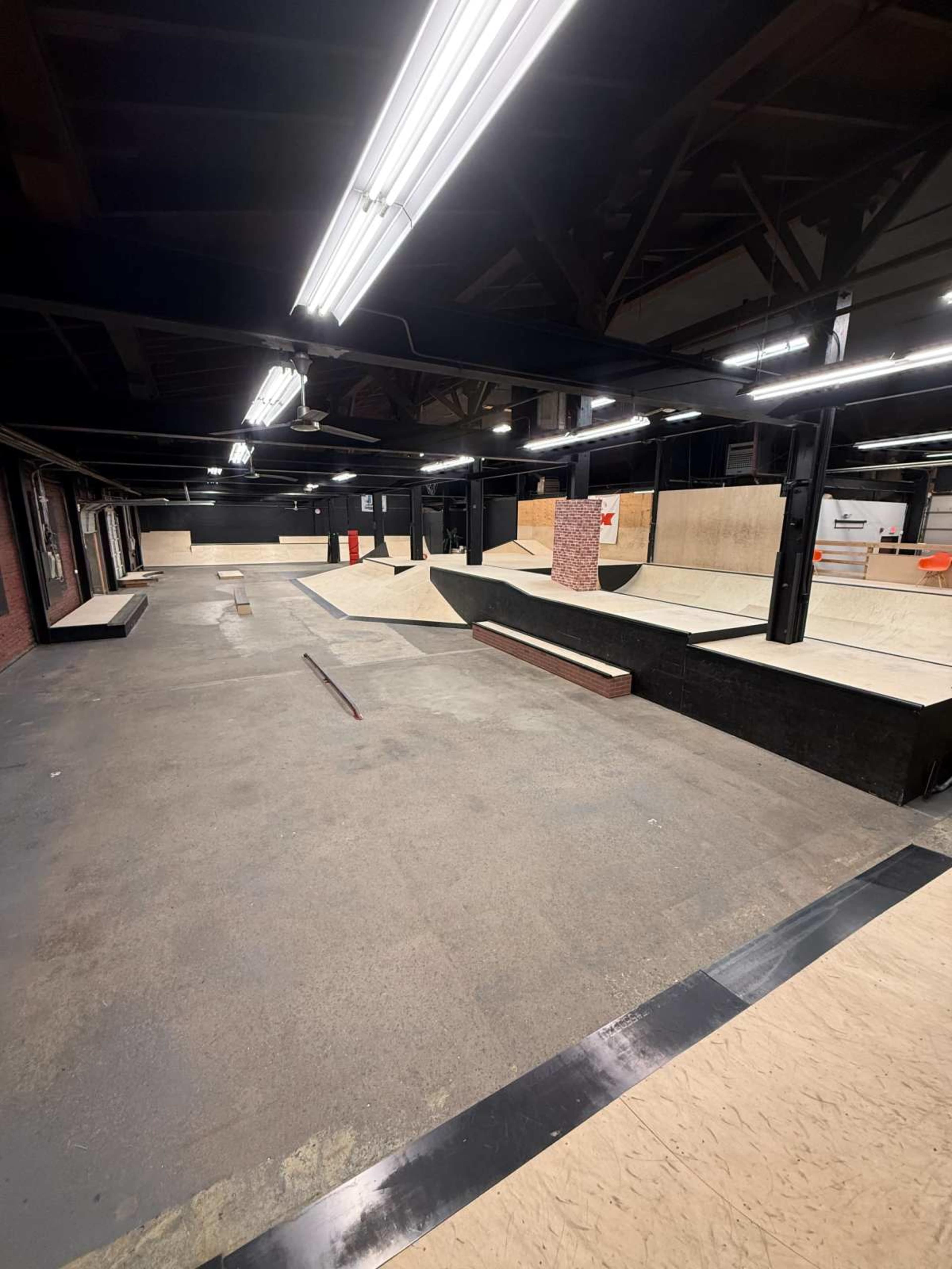 The image shows an indoor skatepark with various ramps, bowls, and rails under bright lighting.