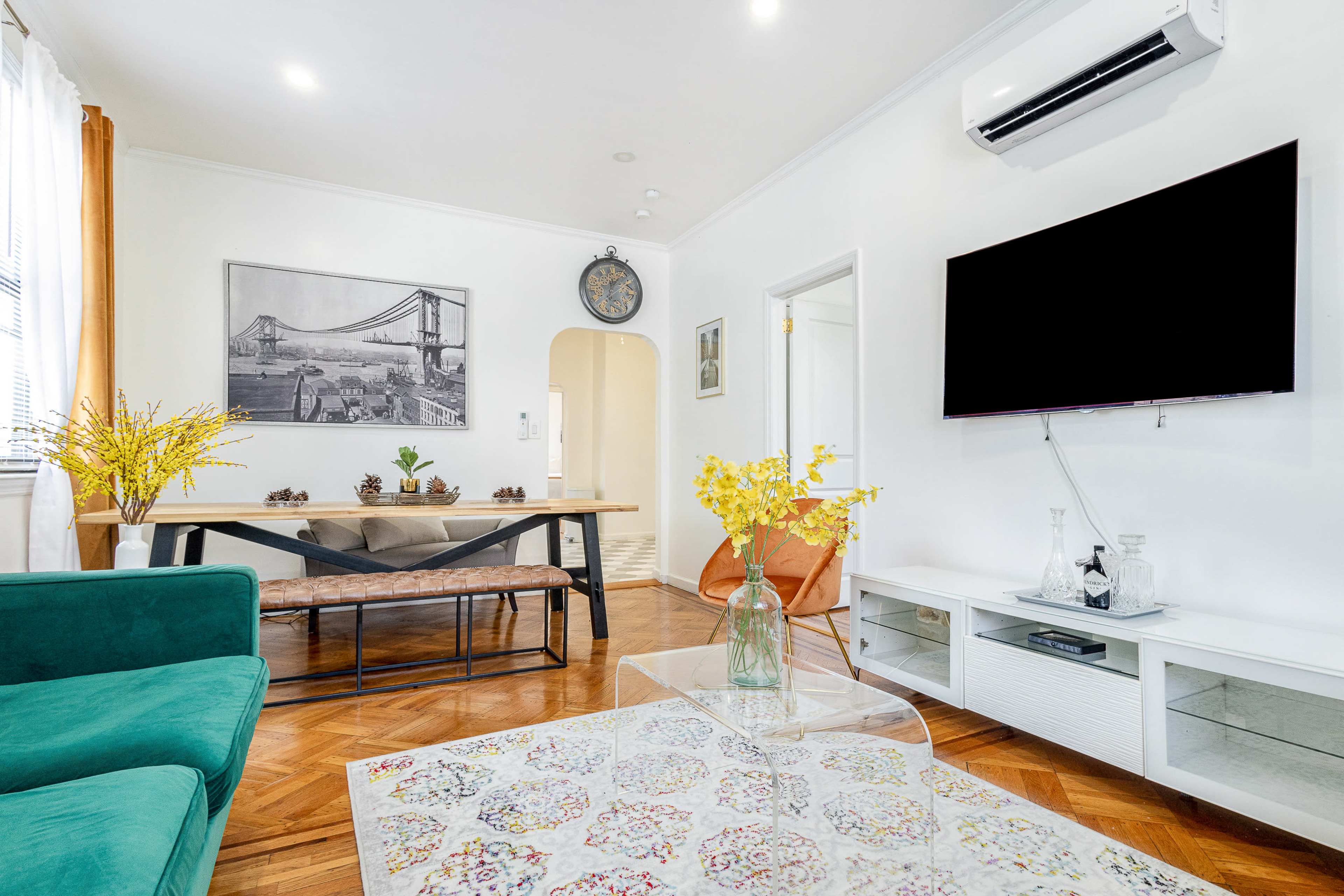 A modern living room with a green couch, a dining area with a table, and a large flat-screen TV mounted on the wall.