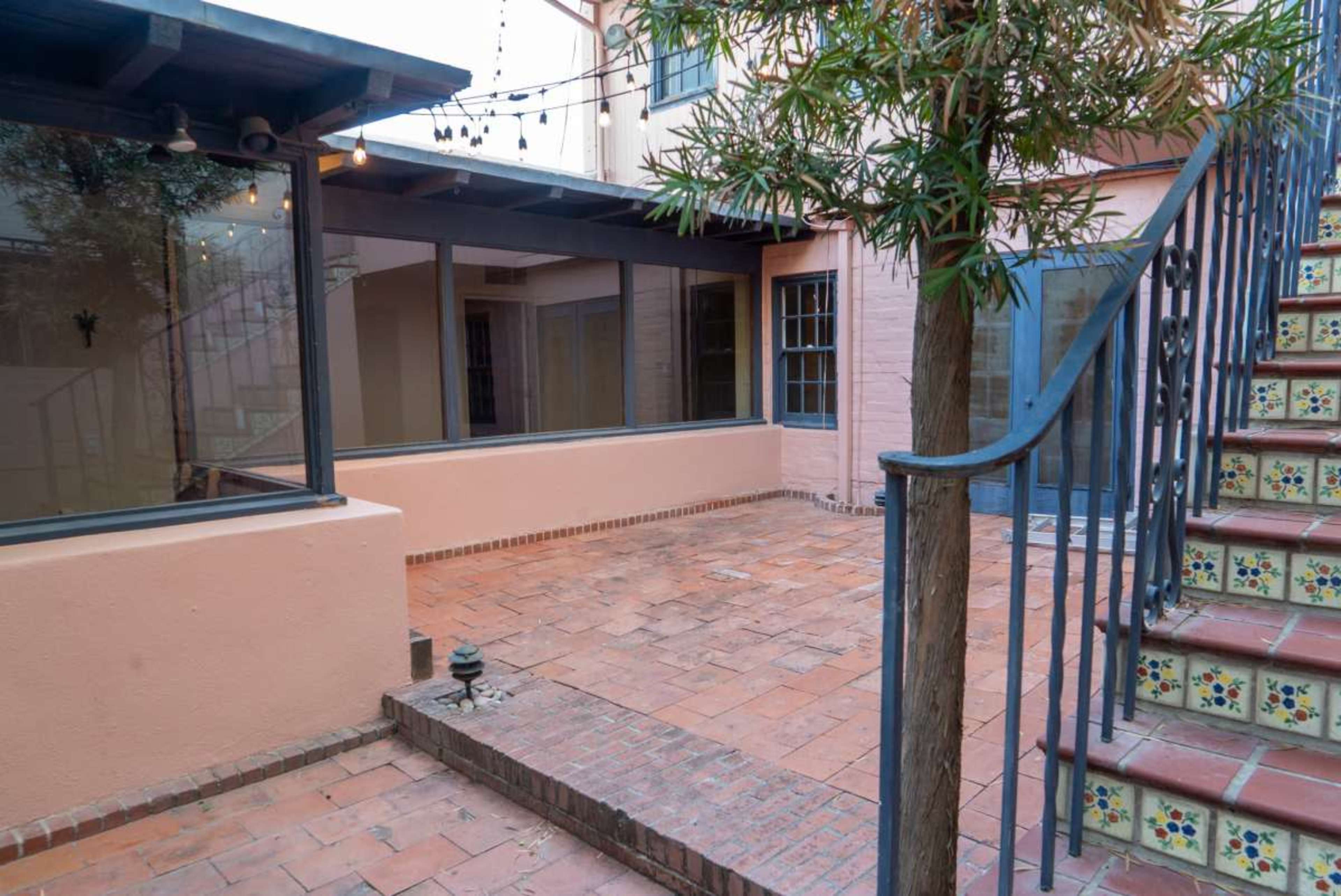 The image shows a patio area featuring terracotta tiles, a decorative stairway with colorful tiles, and a tree near a glass wall.