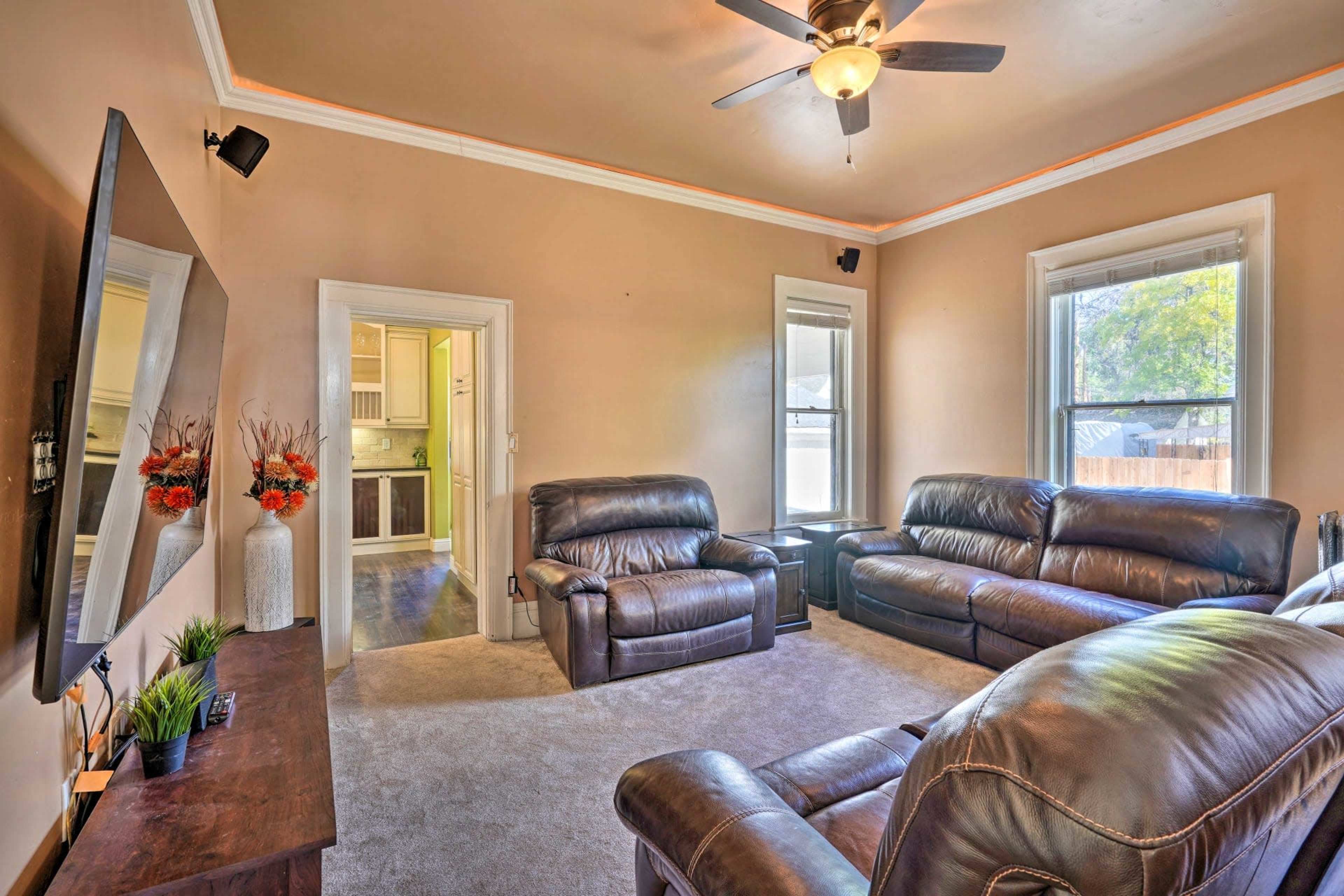A living room with two leather sofas, a TV mounted on the wall, and a doorway leading to another room.
