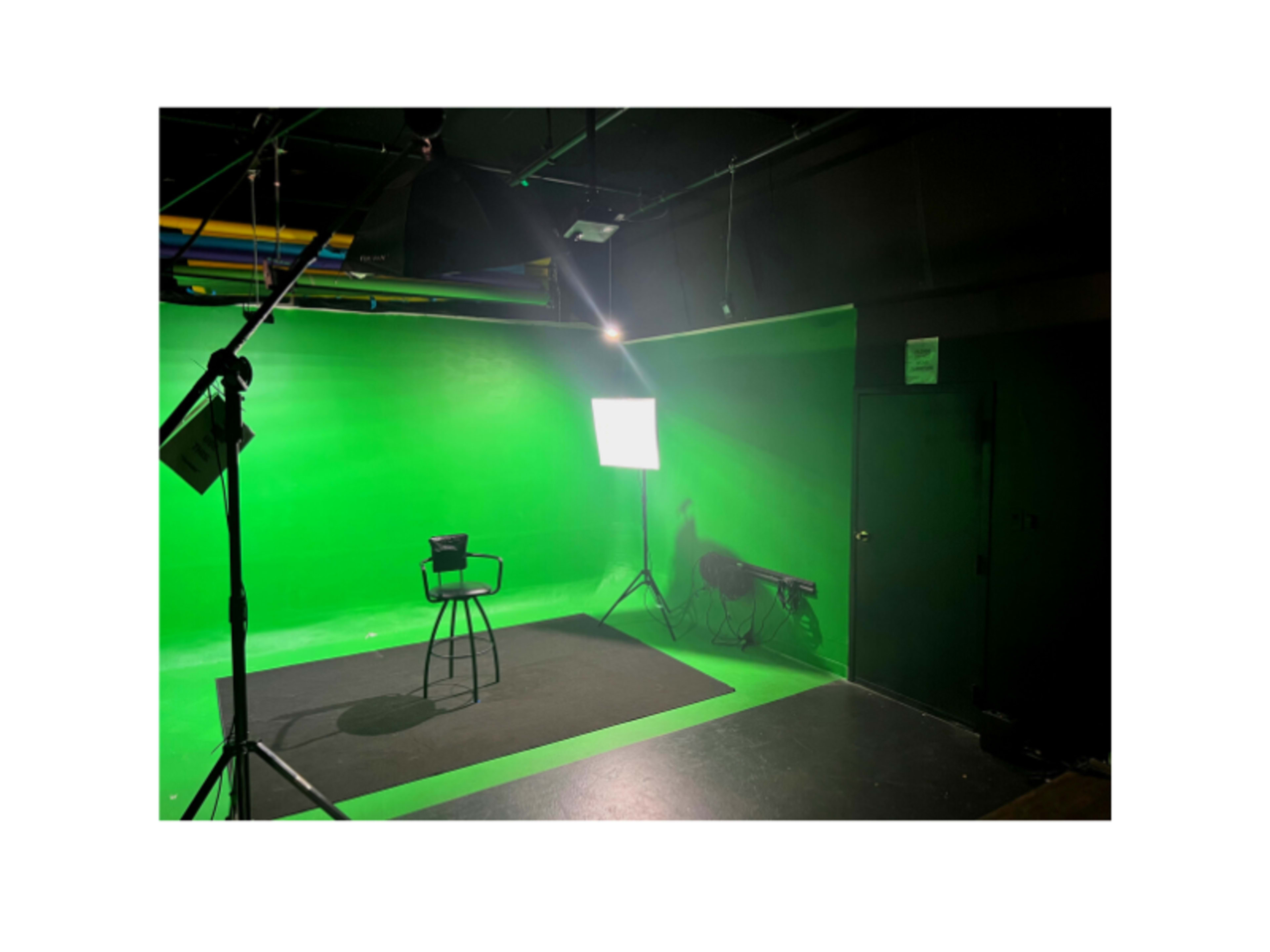 A green screen studio setup with a black stool, lighting equipment, and a dark floor.
