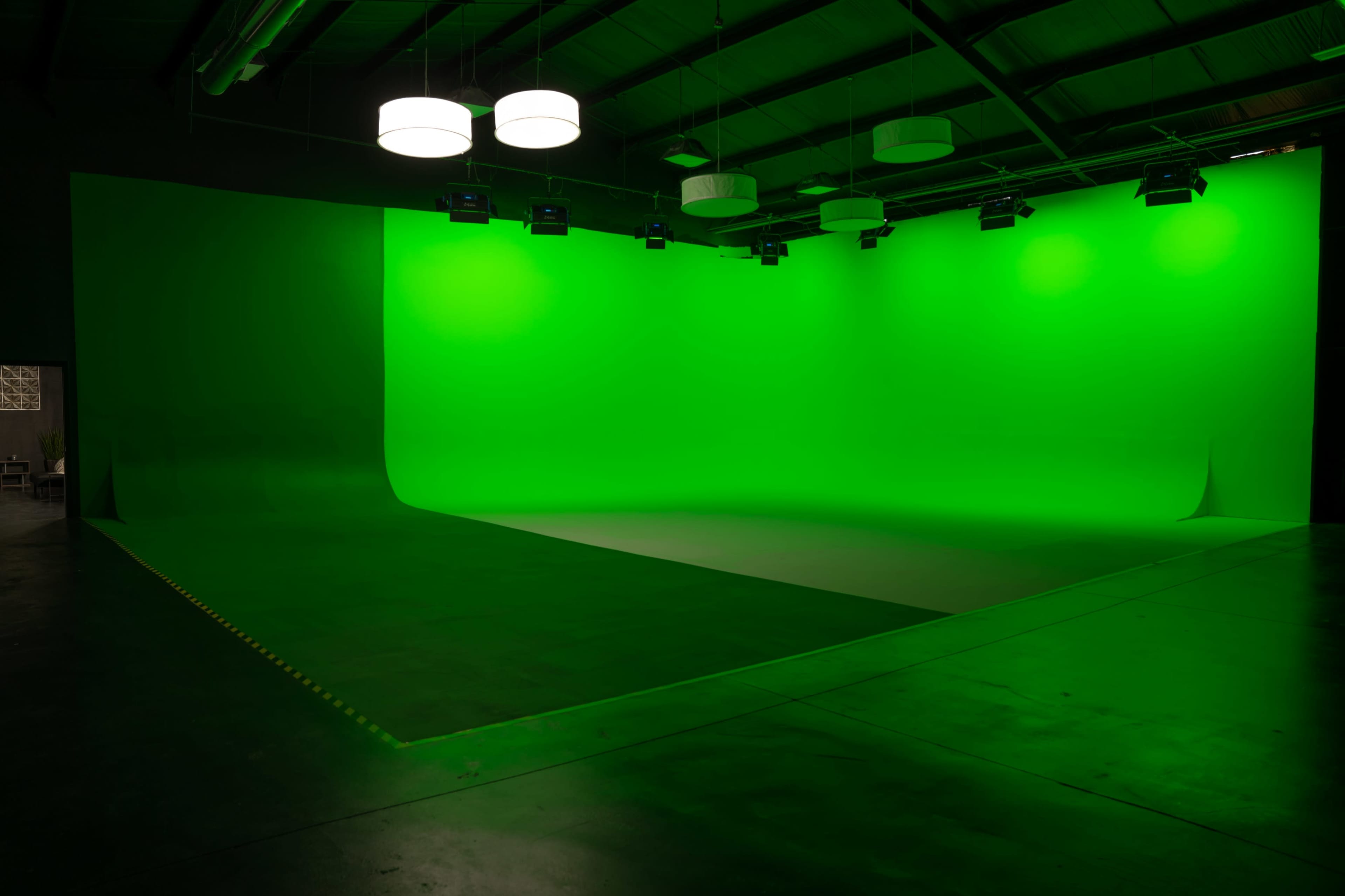A large, empty studio space with a bright green backdrop and overhead lighting.