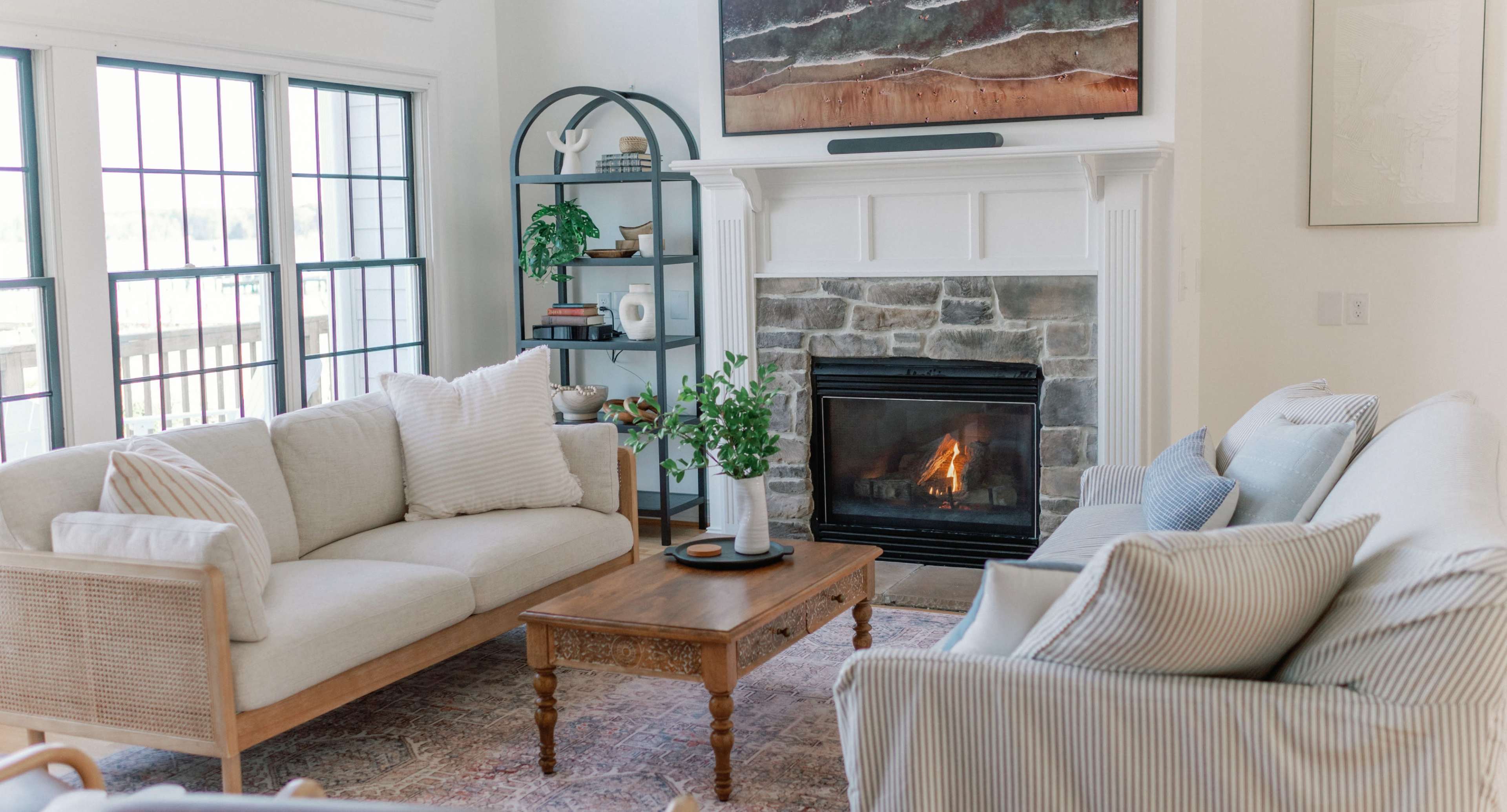 A cozy living room with two sofas facing each other, a wooden coffee table in the center, and a stone fireplace with a small fire burning.