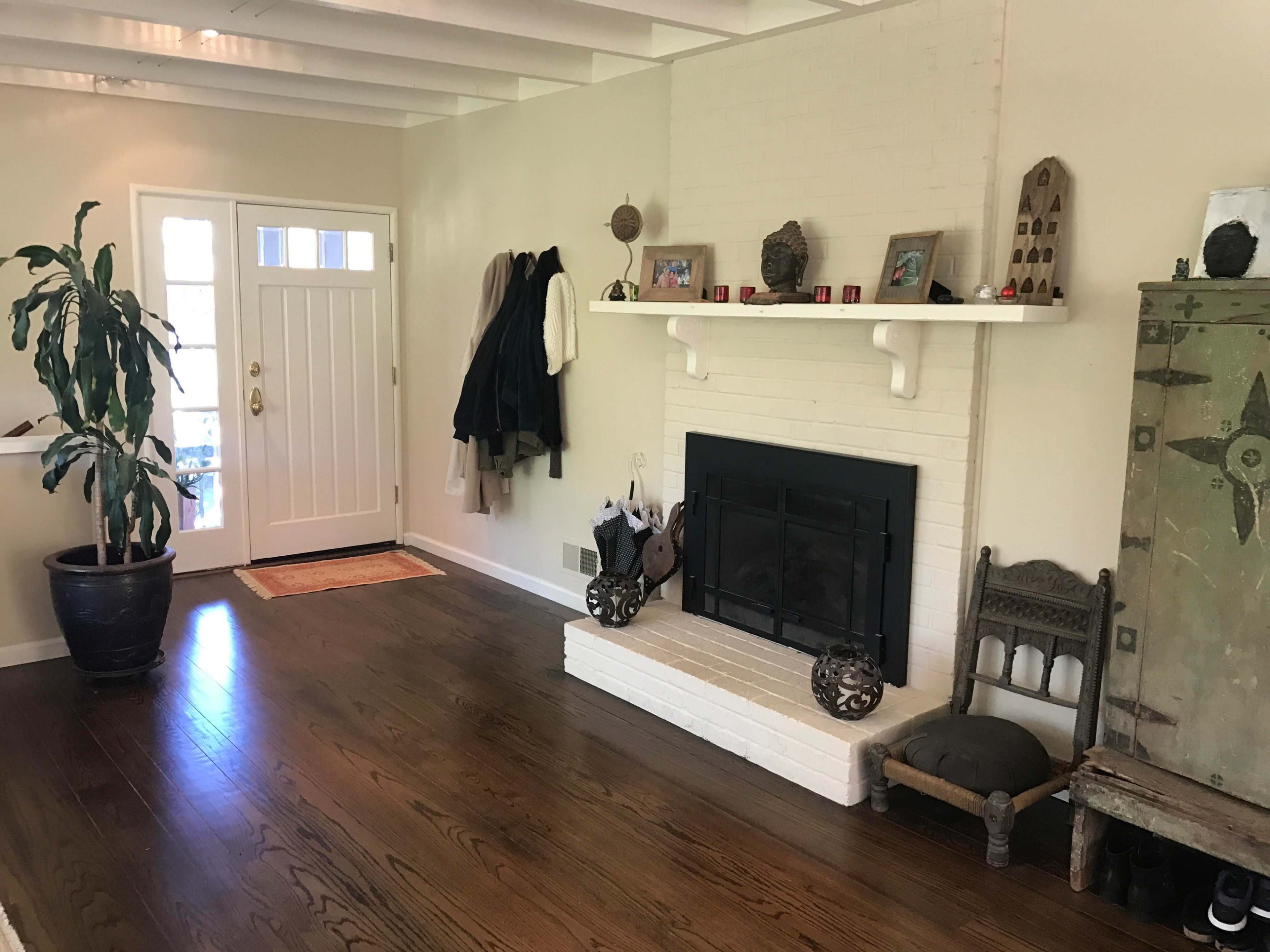 A living room with a fireplace, a coat rack, a potted plant, and a decorative cabinet against a wall.
