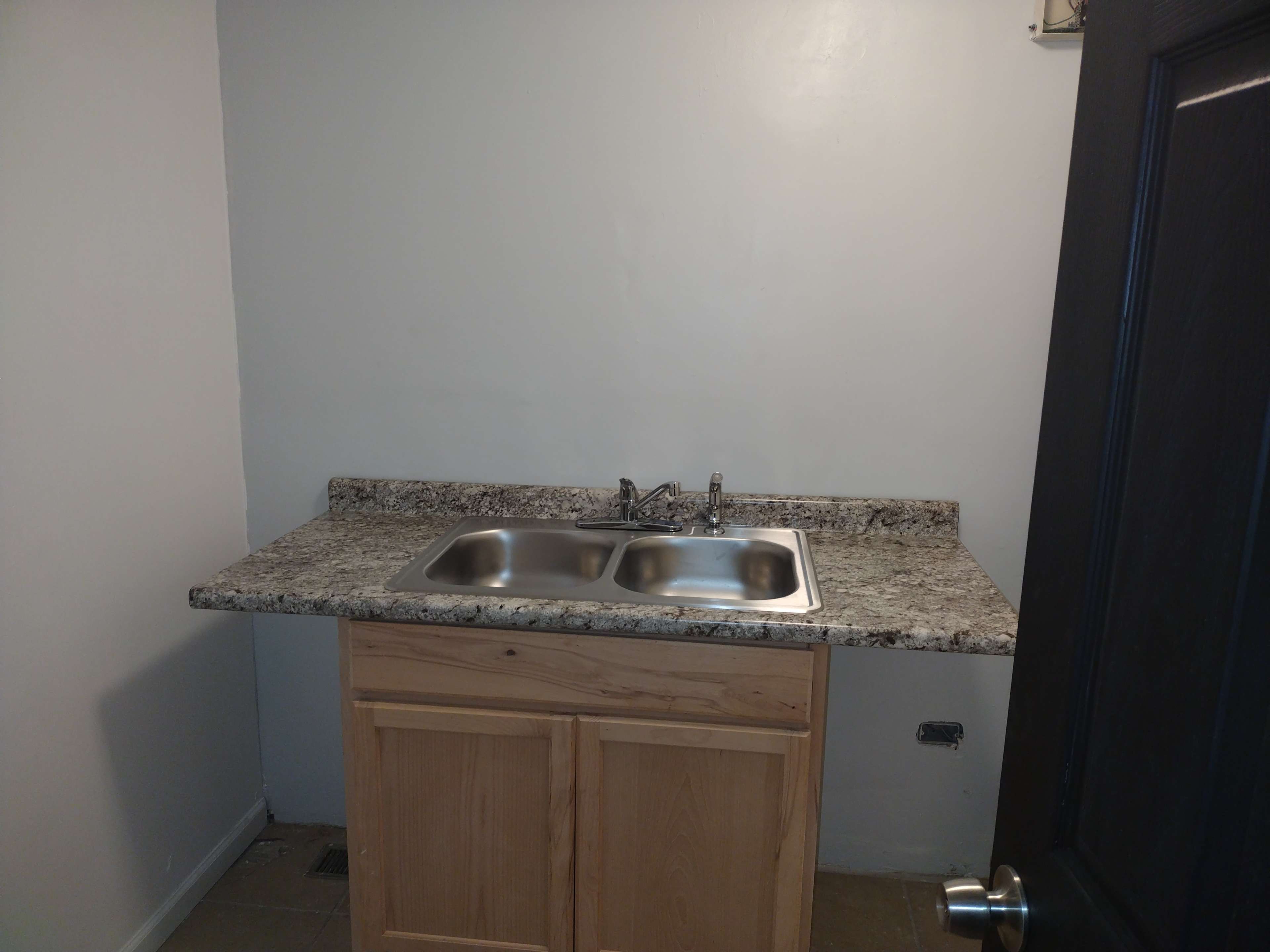 A small kitchenette featuring a double sink with a granite countertop and wooden cabinetry underneath.