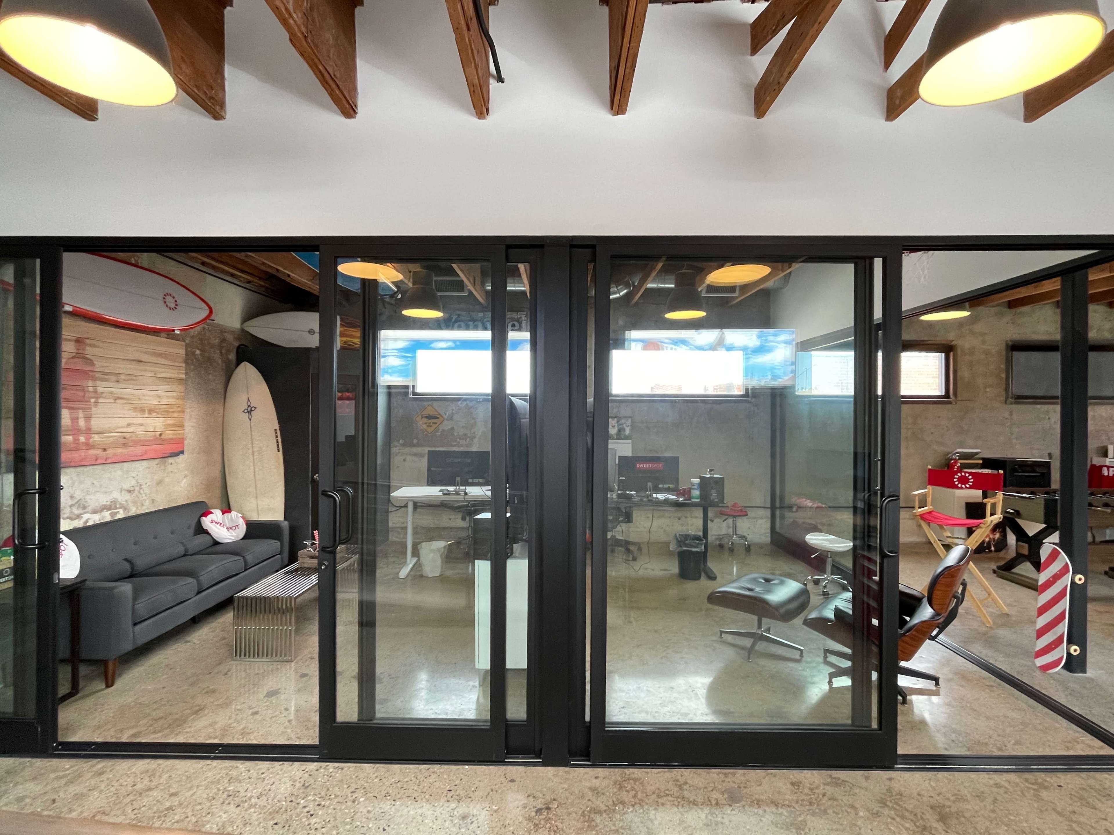 A modern office space featuring glass doors, a seating area with a couch, and workstations equipped with various tools and equipment.