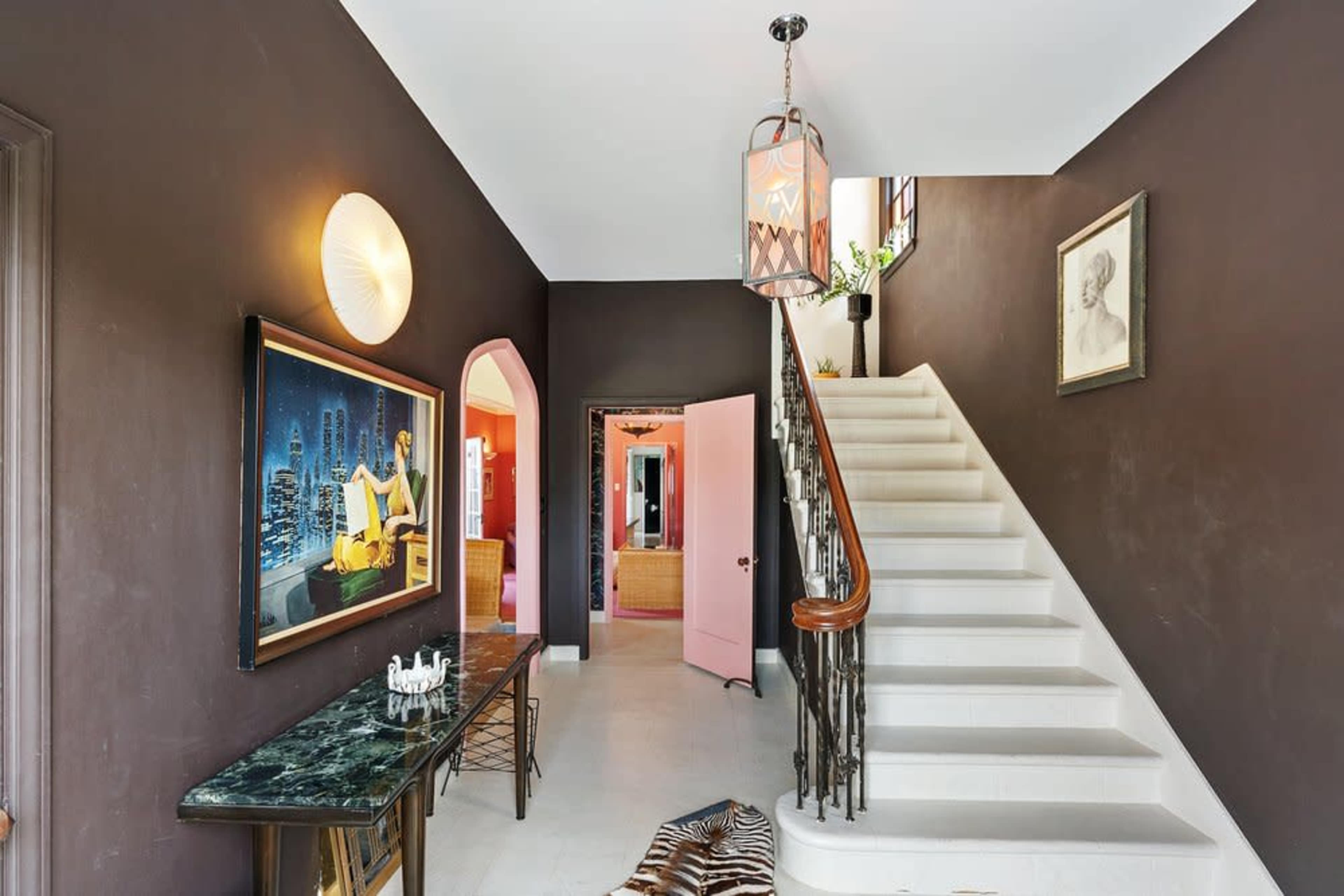 An entrance hall featuring a staircase, a dark wall with artwork, and a decorative light fixture.