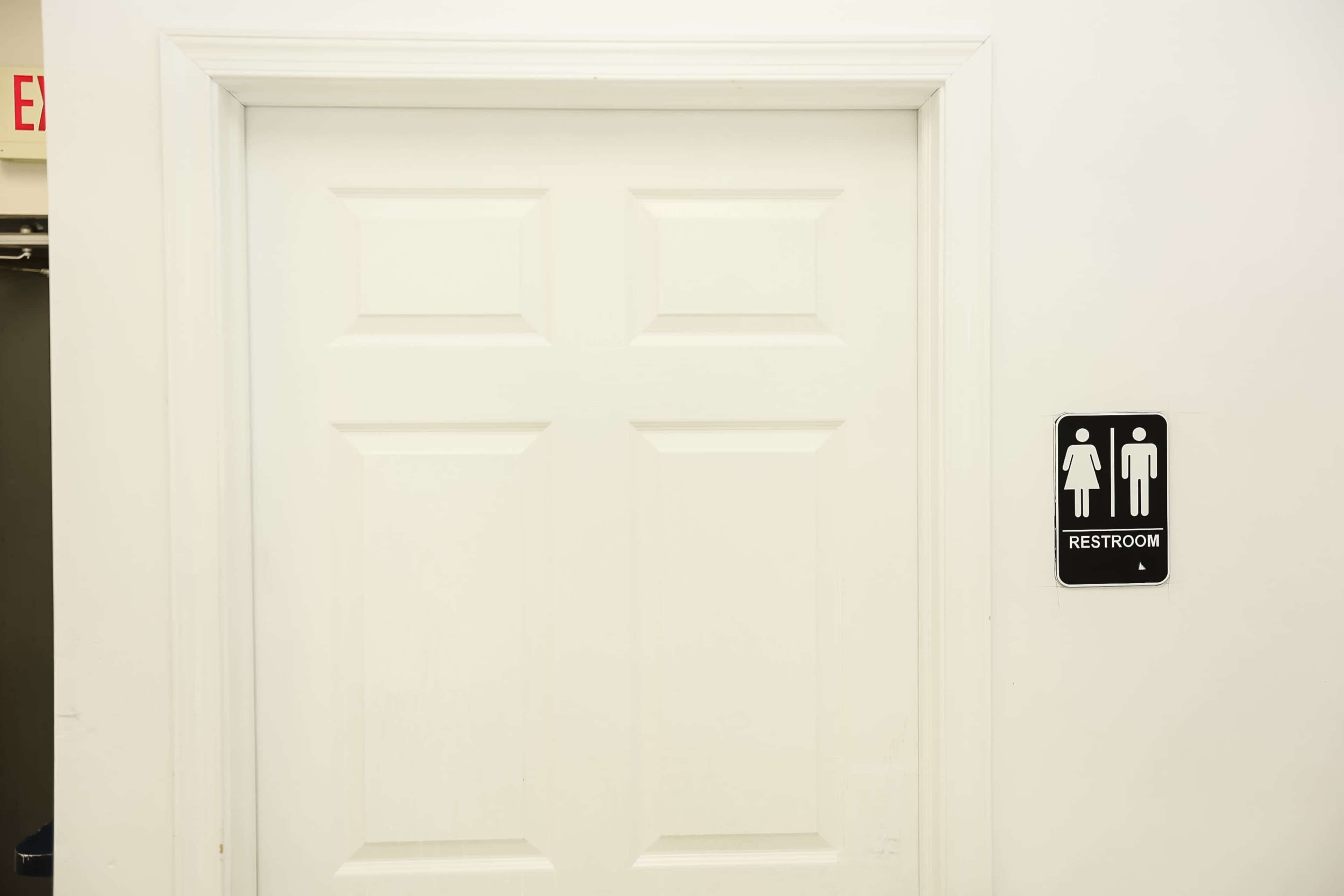 A closed white door with a sign indicating the location of a restroom.
