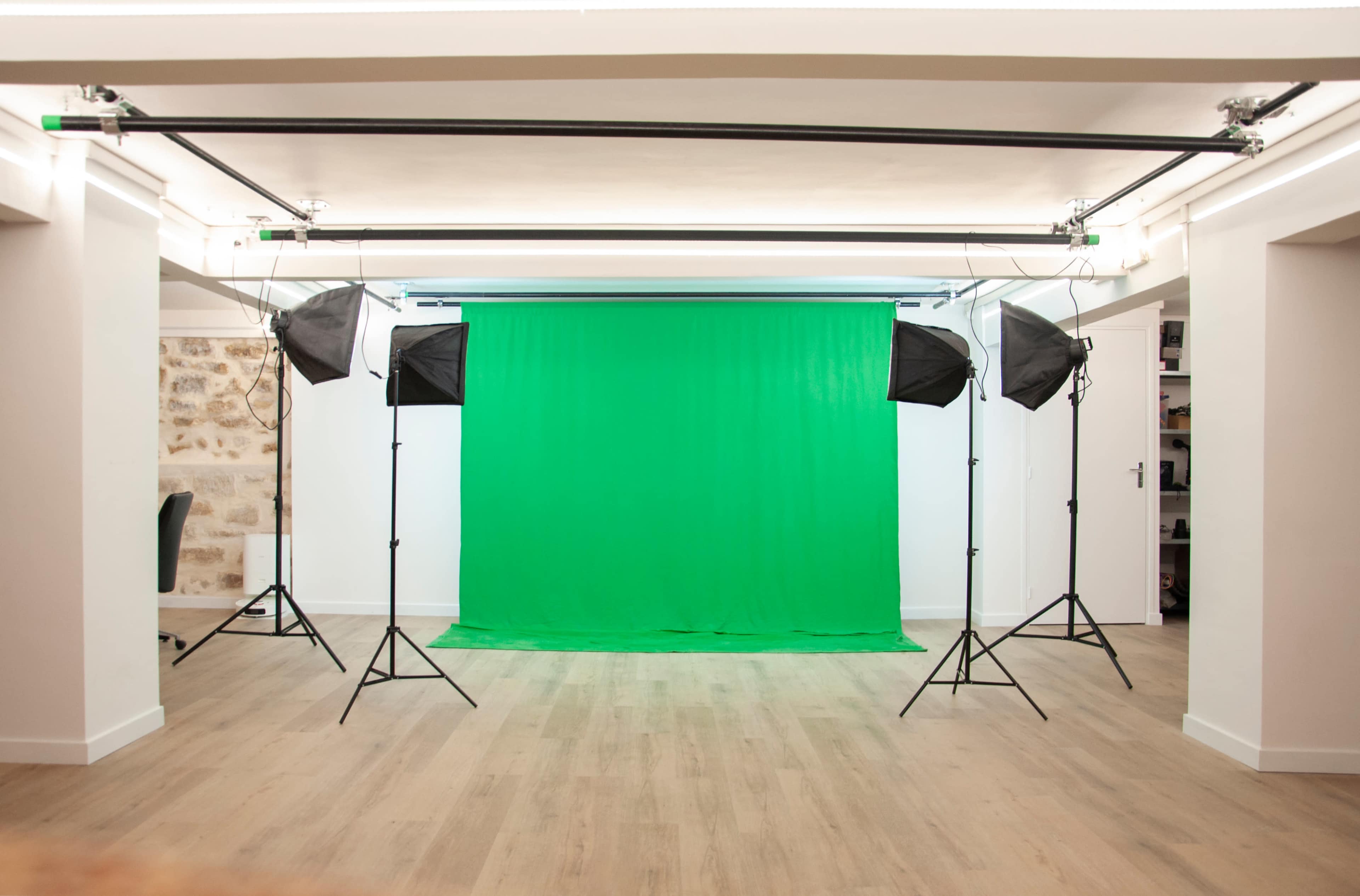A photography studio features a green backdrop surrounded by four lighting softboxes on tripods.
