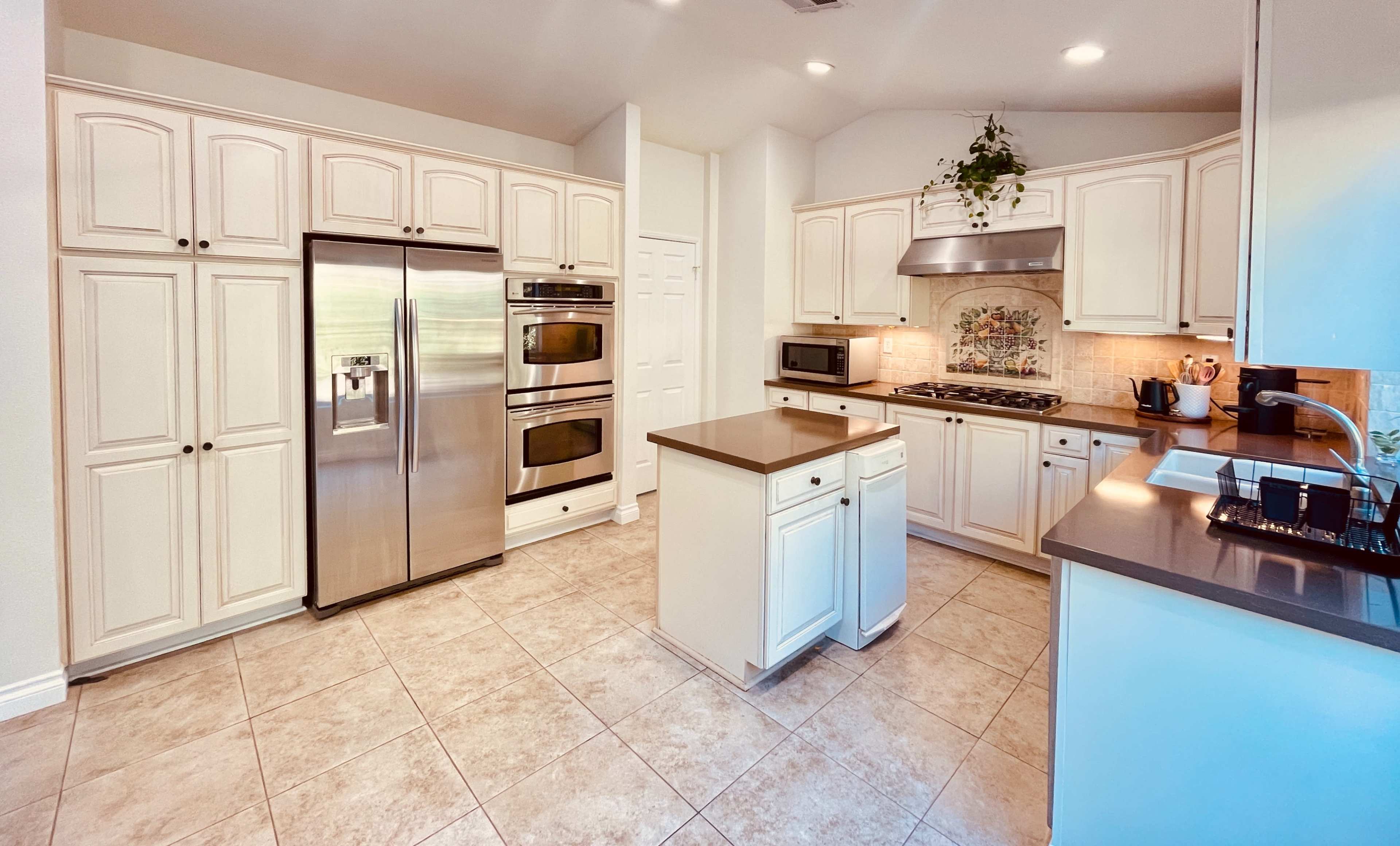 A modern kitchen with white cabinetry, stainless steel appliances, and a tile floor.