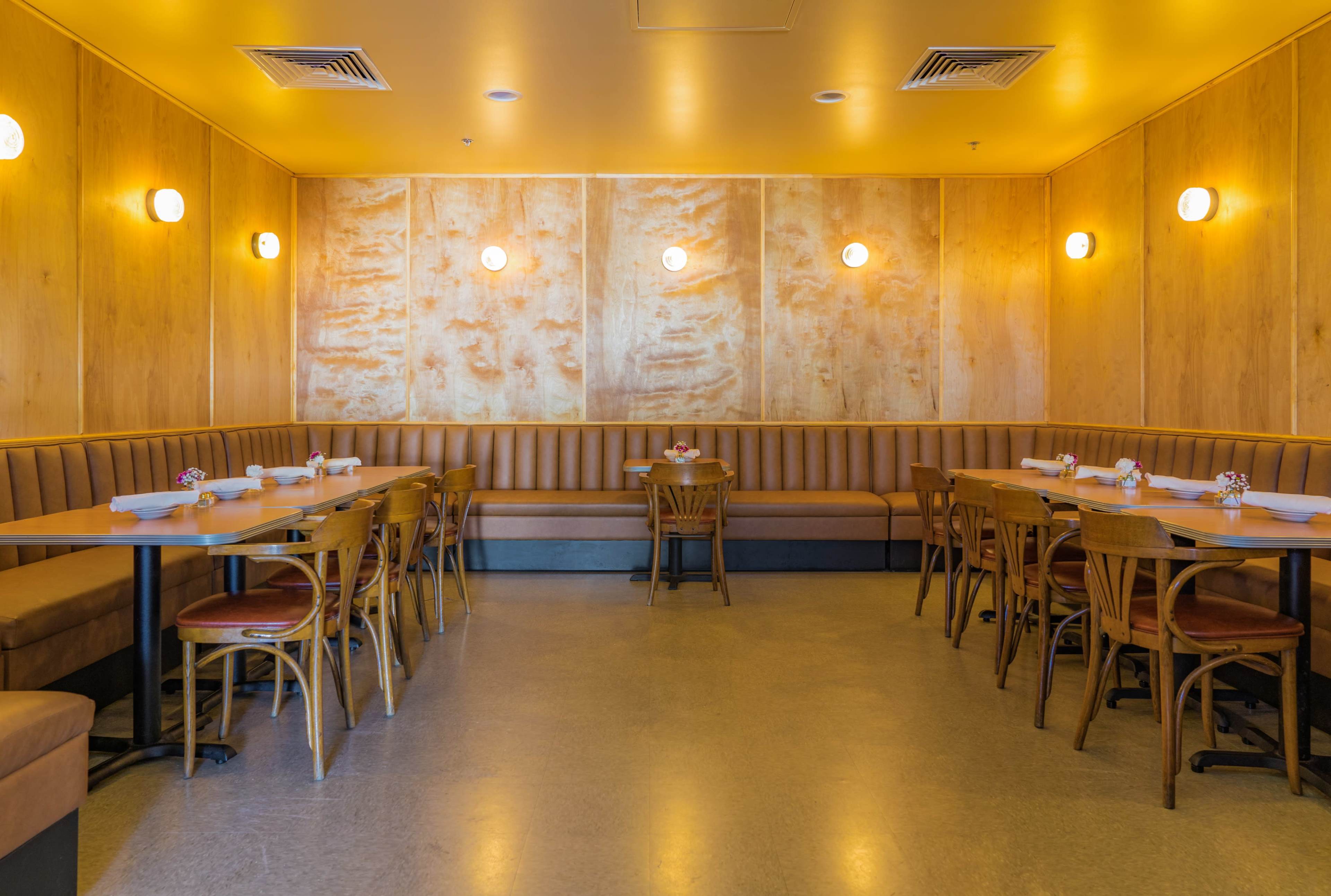 The image shows a restaurant interior with wooden paneling, booth seating, and tables neatly set for dining.