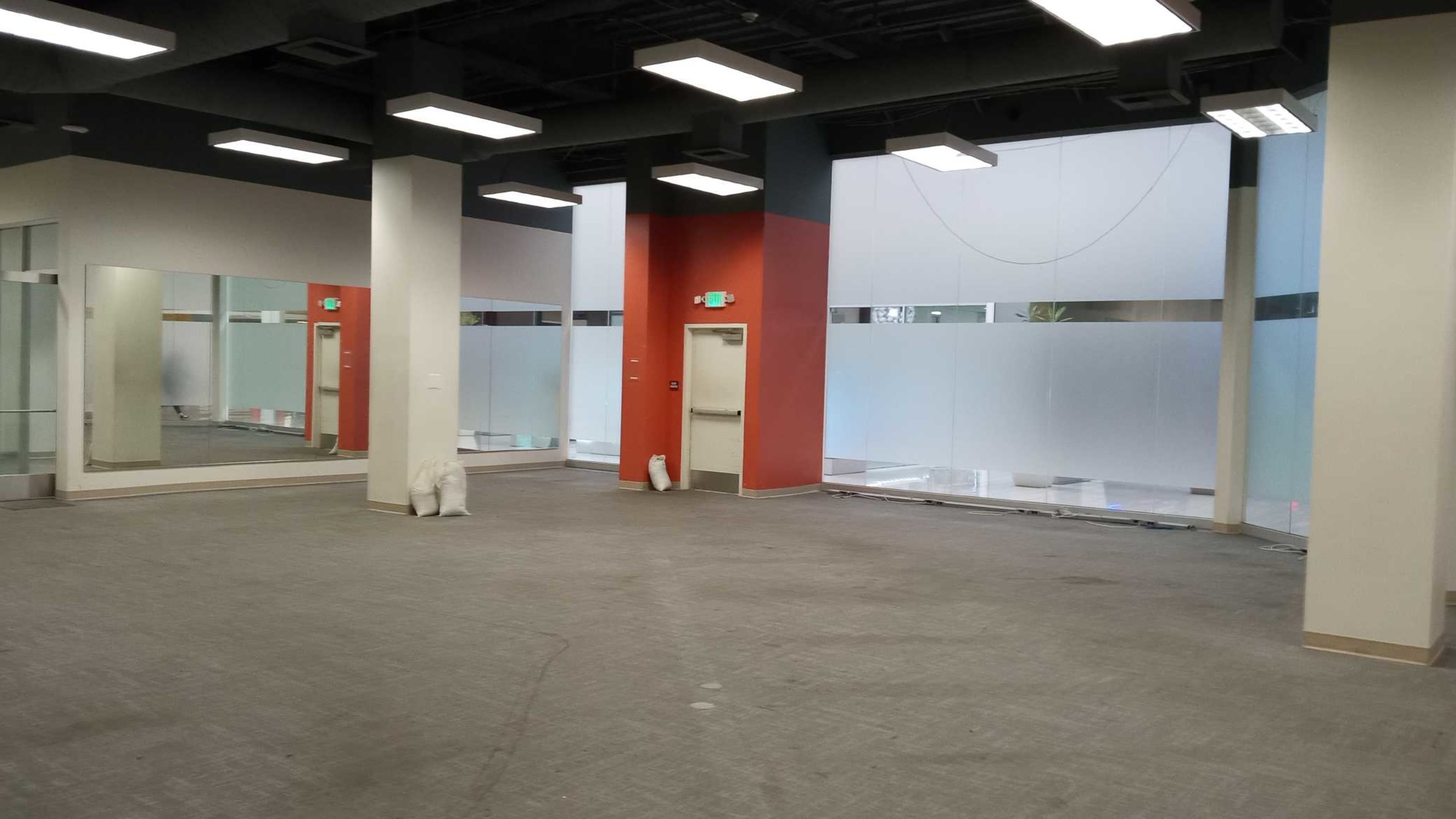 An empty commercial space with concrete flooring, large windows, and white and red walls.