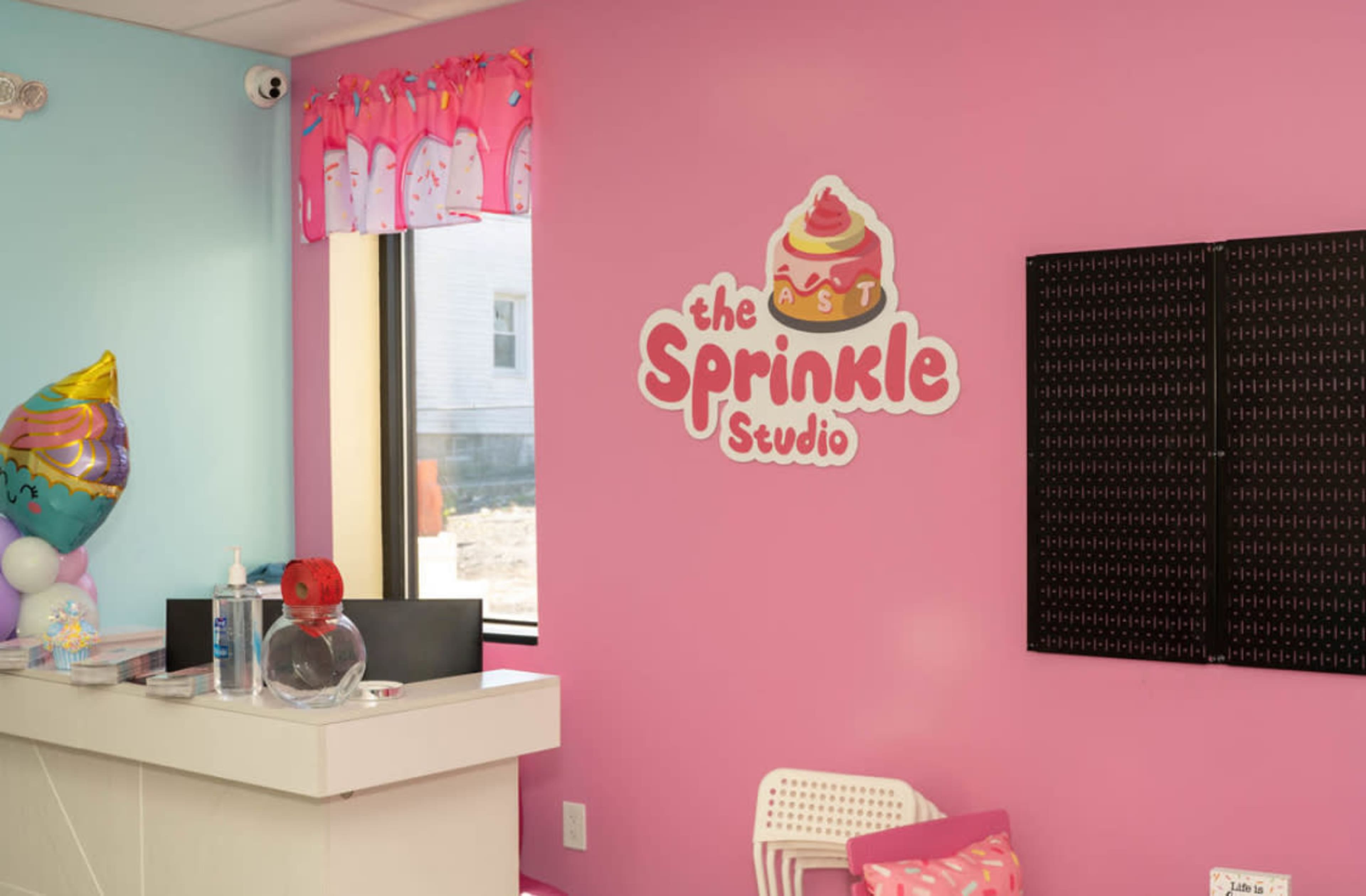 The interior of a brightly colored studio features a pink wall with a logo that reads "the Sprinkle Studio" and a reception area with a white counter.