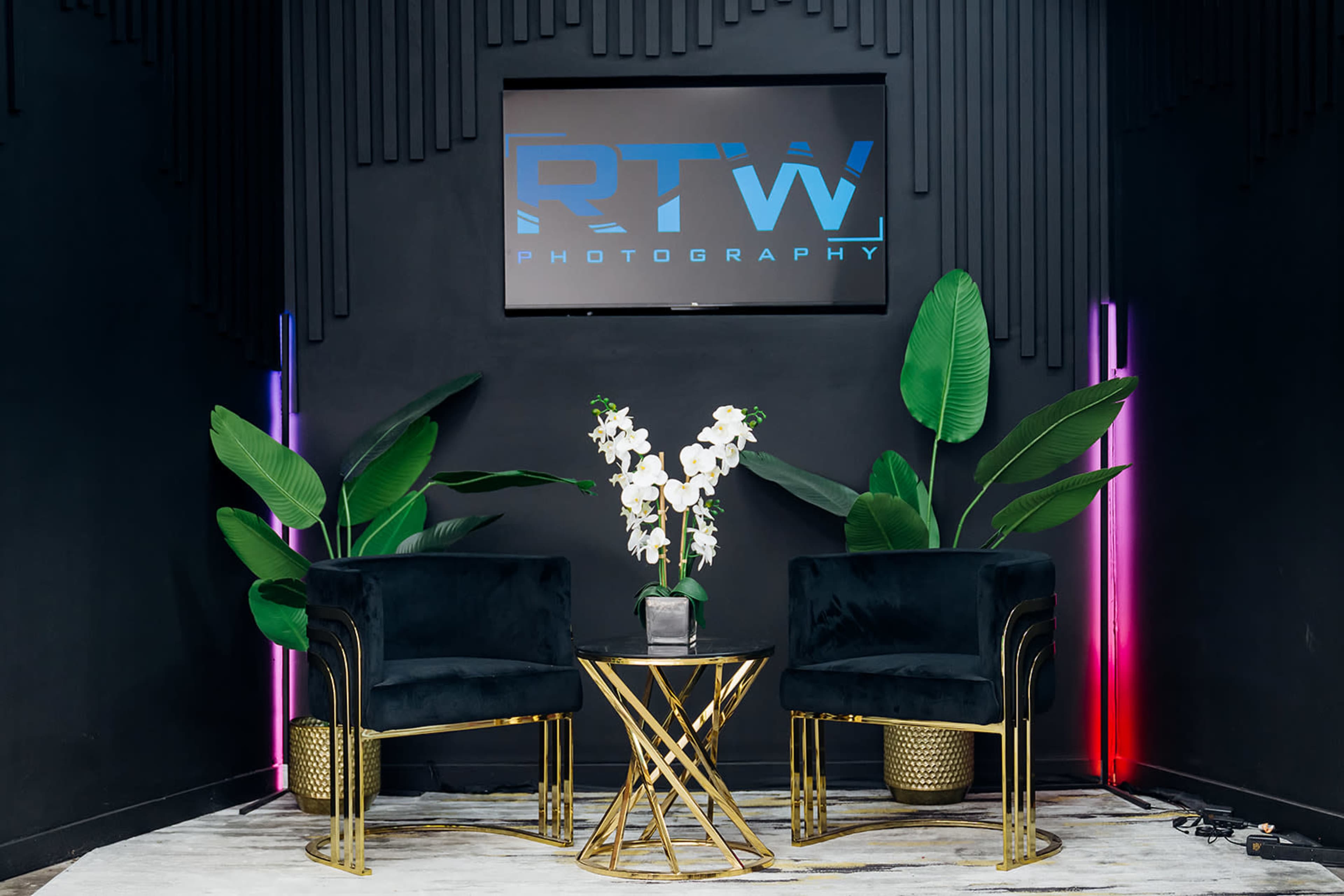 The image features a modern photography studio setup with two black chairs, a round gold table, and large potted plants, set against a black wall displaying the "RTW Photography" logo.