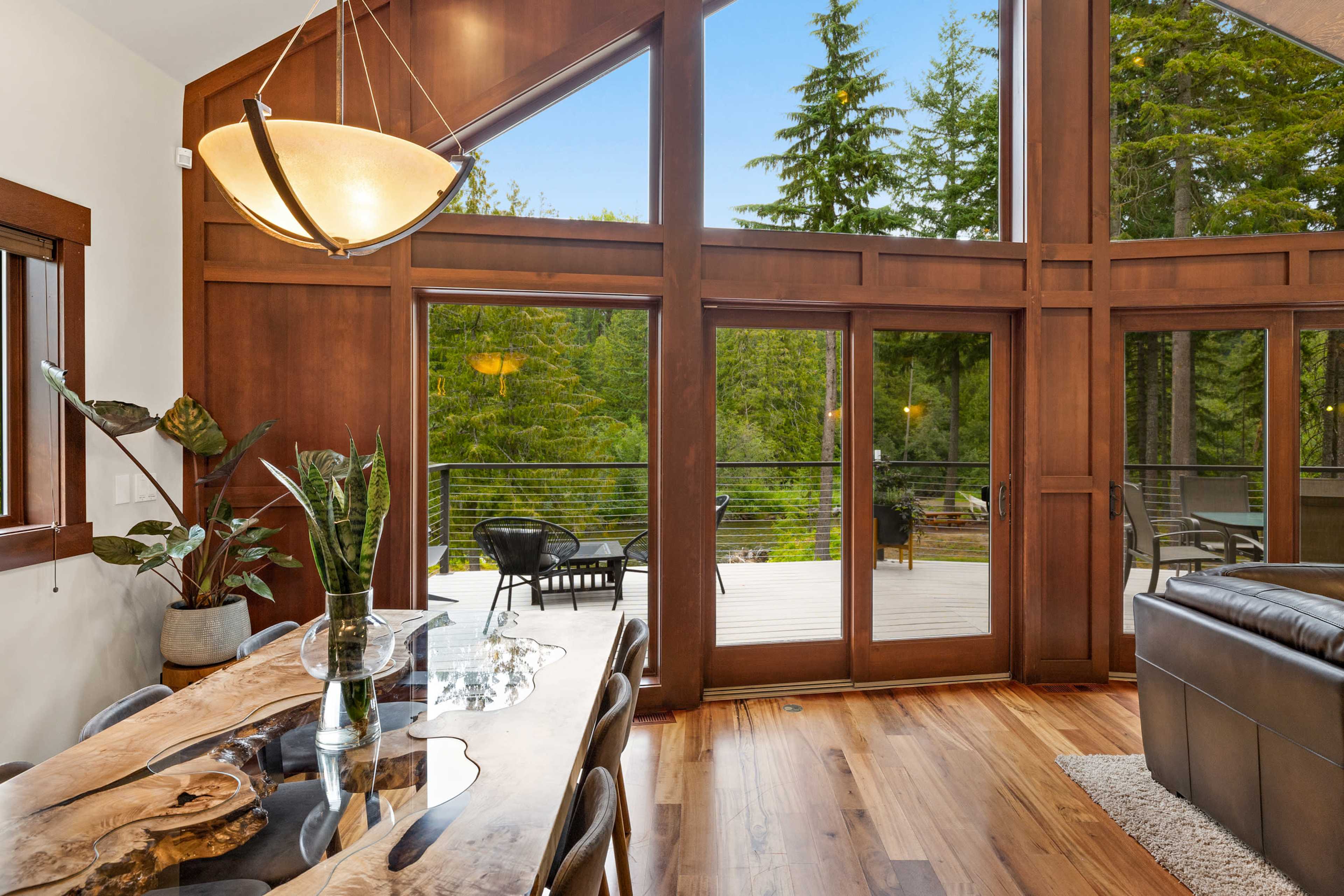 A modern dining area with a wooden table and large windows overlooking a forested outdoor deck.