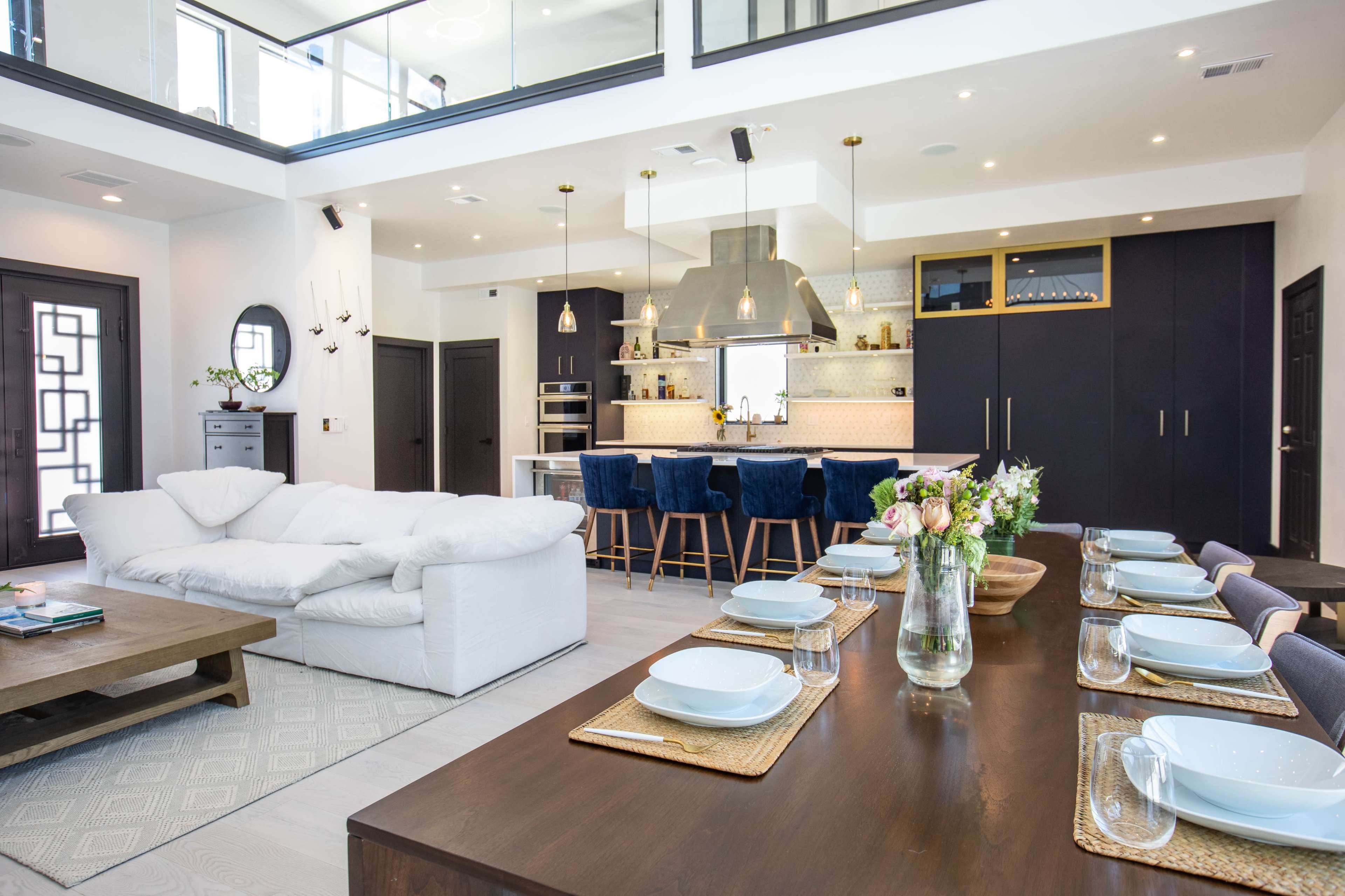 A modern open-concept living and dining area with a white sofa, a wooden dining table set for eight, and a kitchen featuring a large island and bar seating.