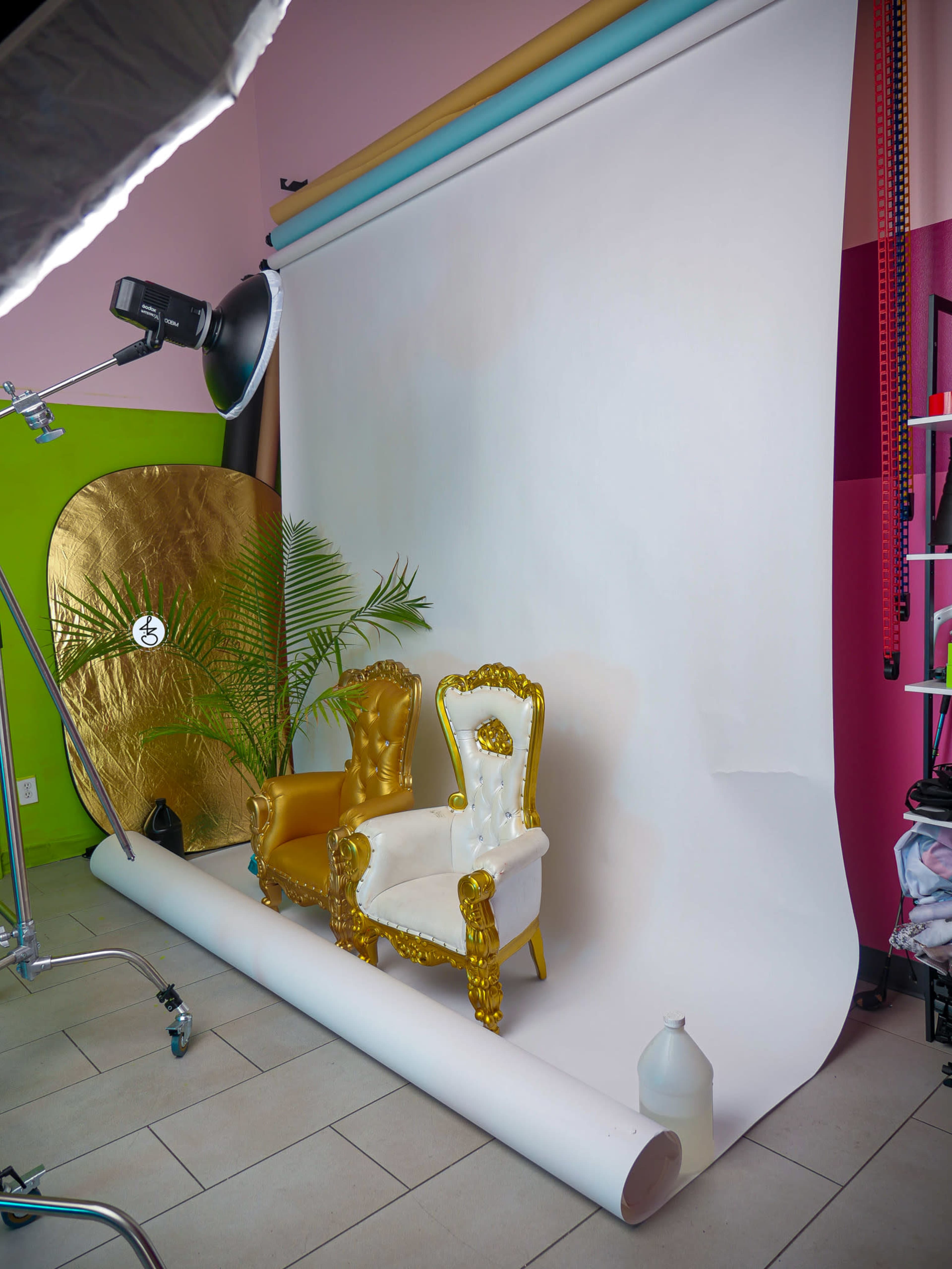 The image shows a photography studio setup with two ornate chairs, one gold and one white, in front of a white backdrop.