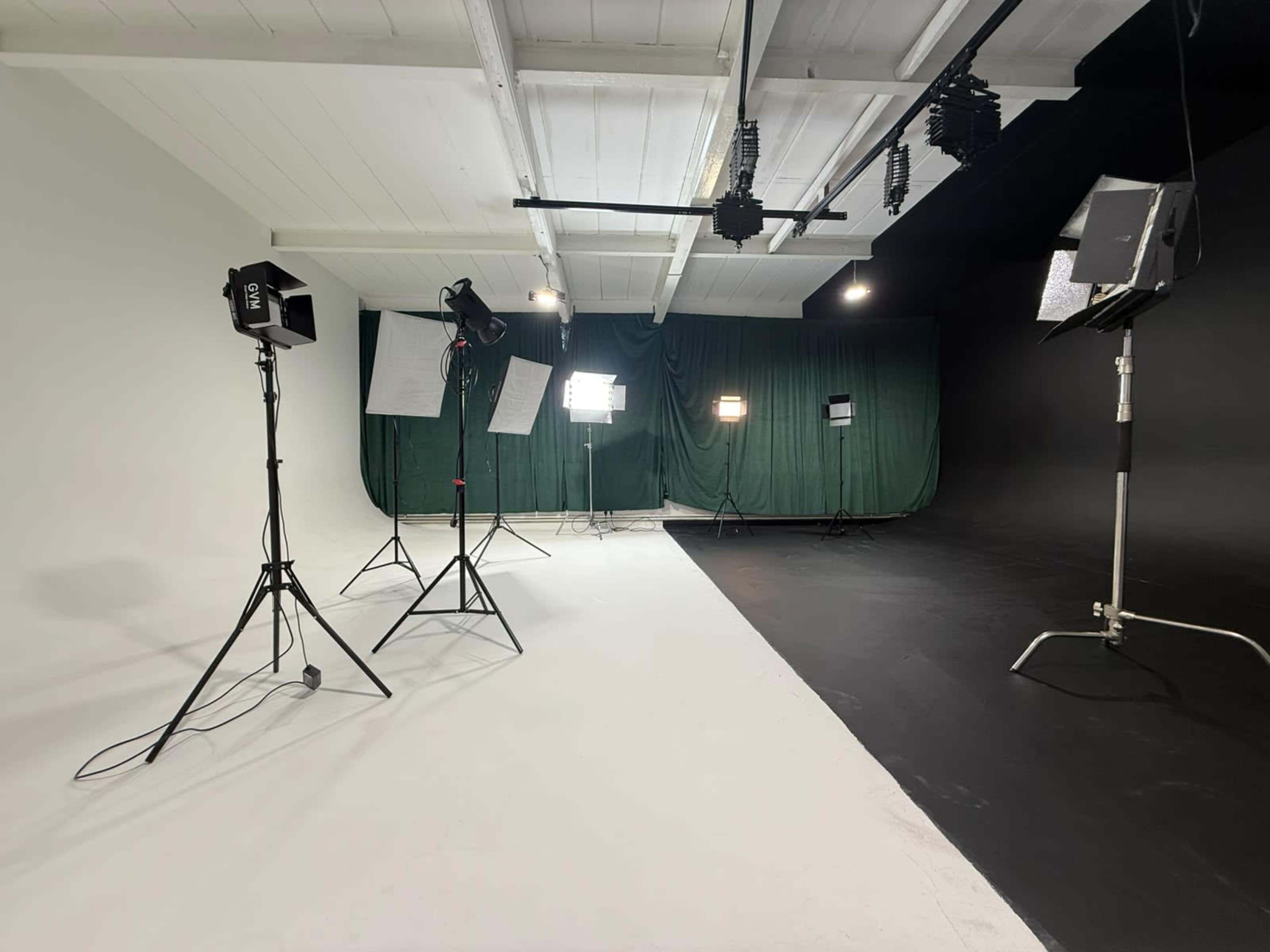 The image shows a photography studio with a white and black background, equipped with various lighting fixtures on stands.