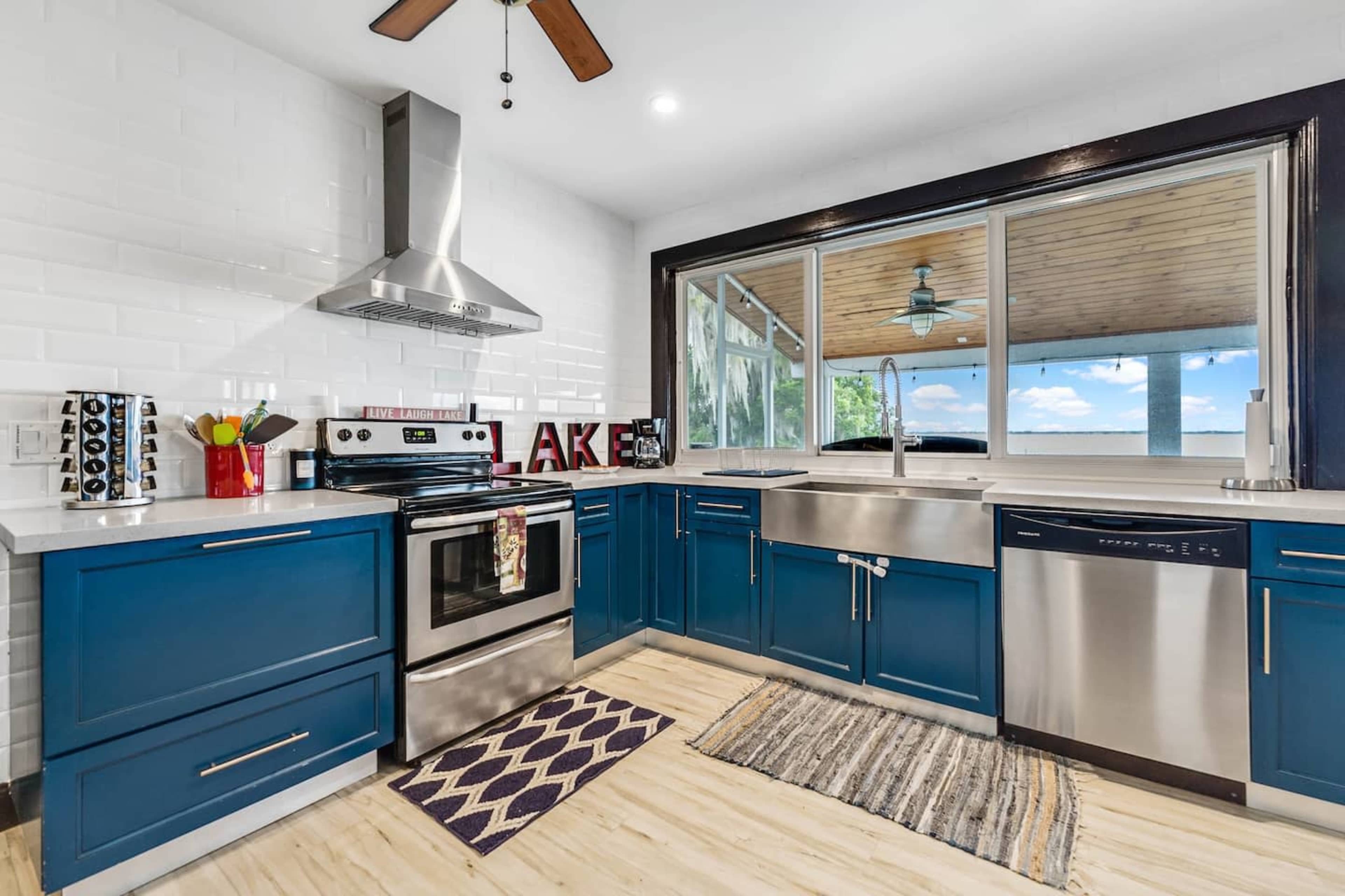 A modern kitchen features blue cabinets, stainless steel appliances, and a large window overlooking a patio.