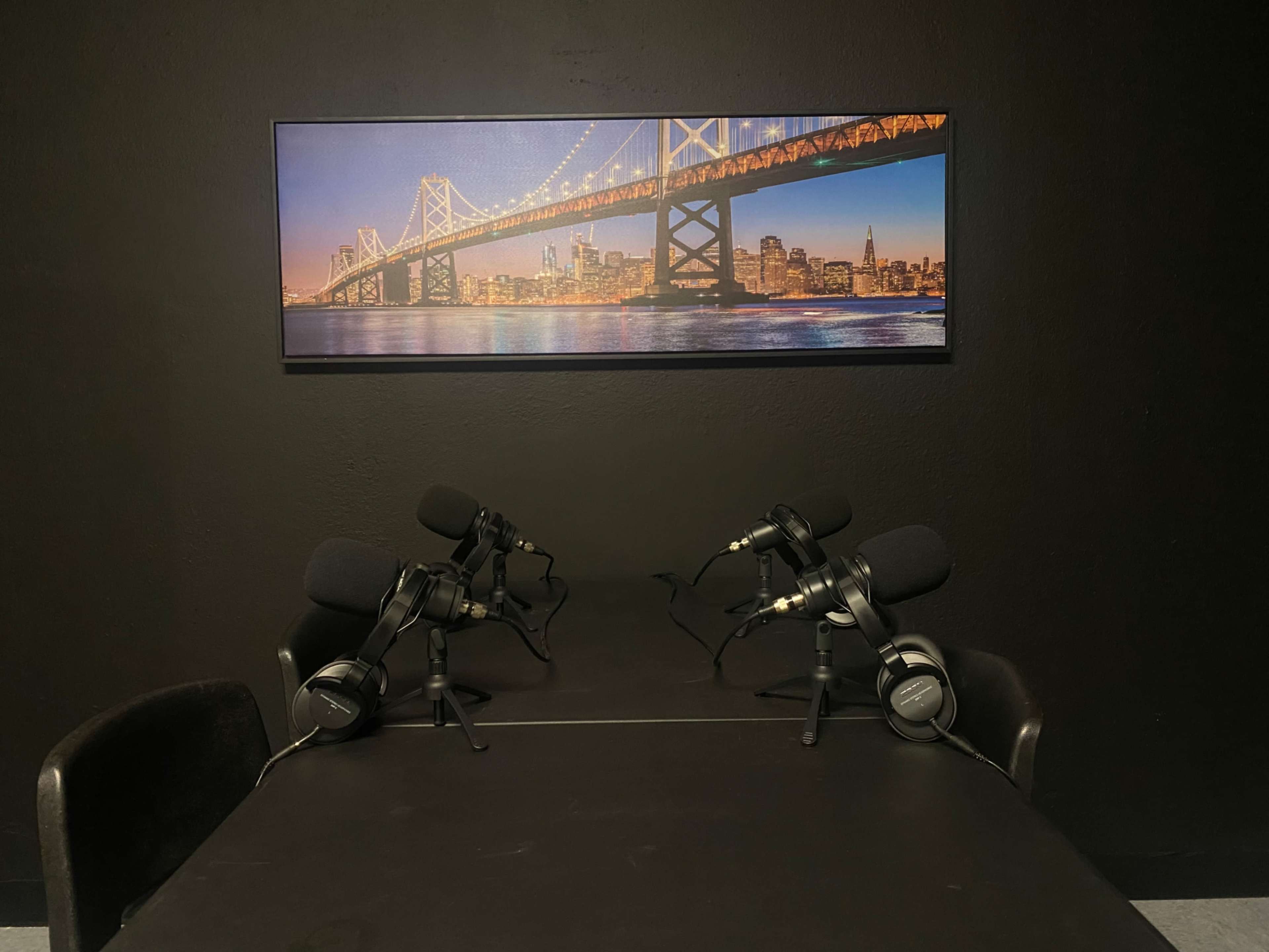 A table with two microphones positioned on either side, set against a backdrop featuring a city skyline and a bridge.