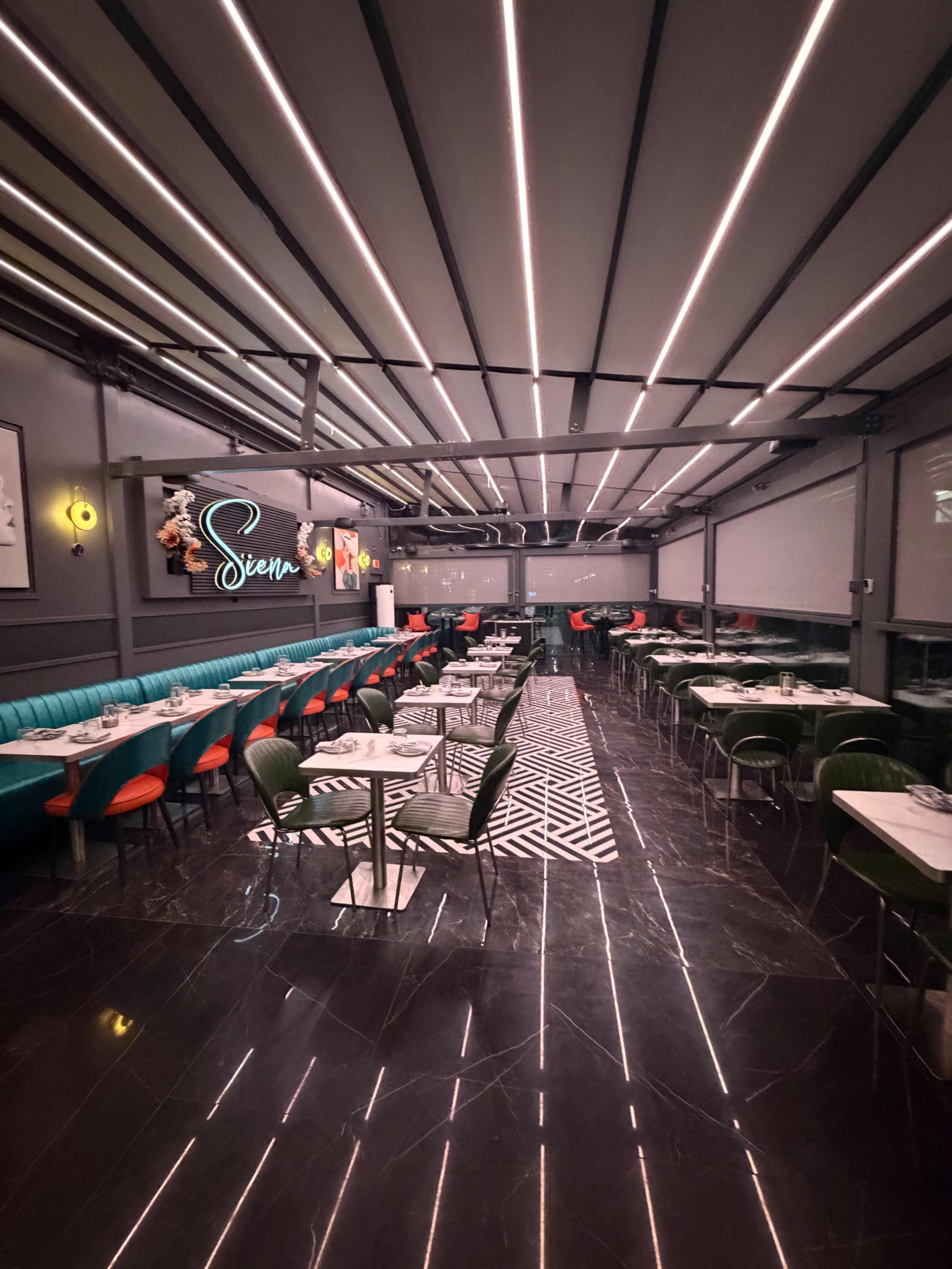 The image shows the interior of a modern restaurant featuring teal and red seating, sleek tables, and a stylish geometric floor design illuminated by overhead lighting.