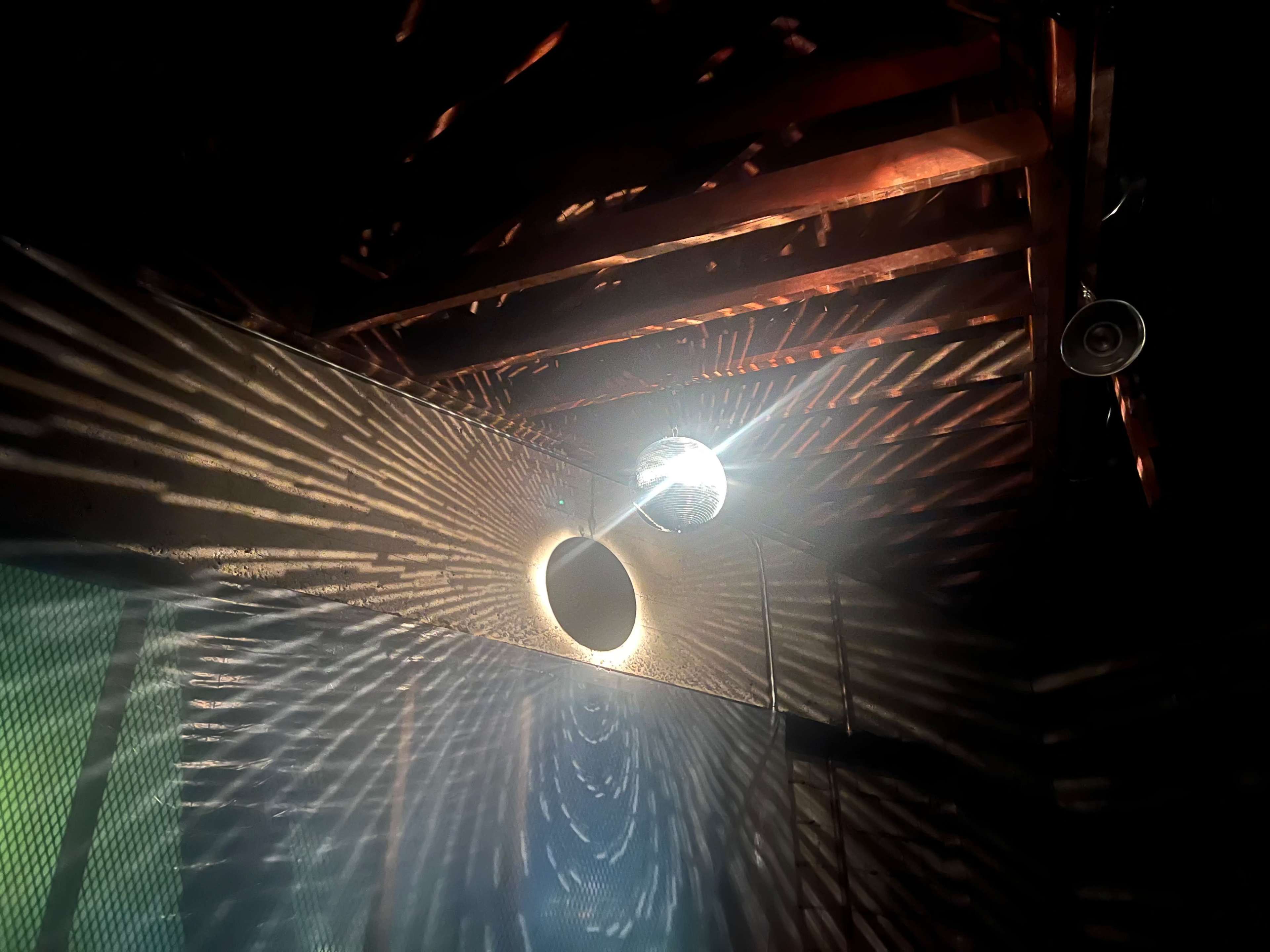 A disco ball casts patterned light onto the wall and ceiling of a dimly lit room.