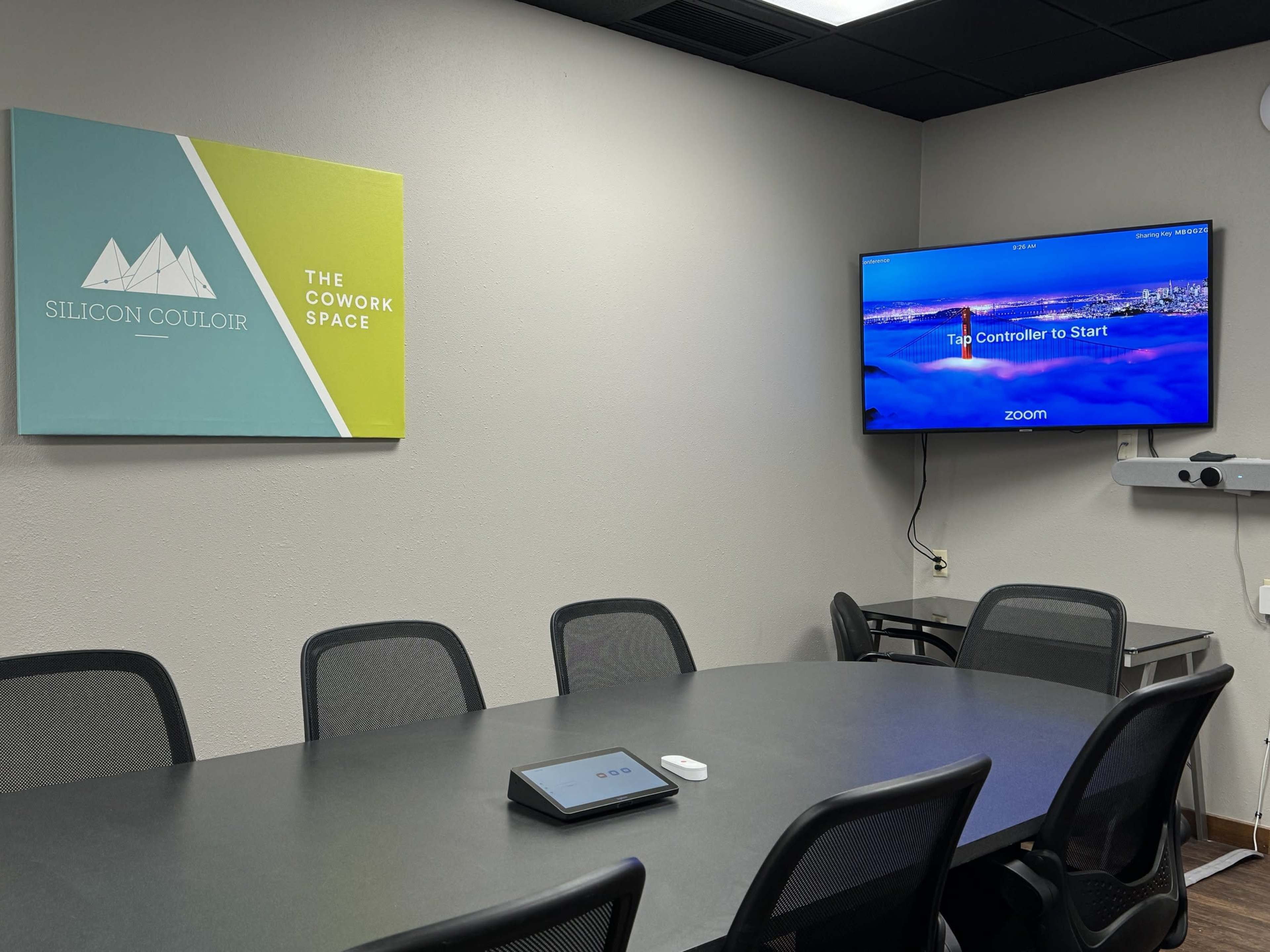 The image shows a conference room with a large table, multiple black chairs, a mounted television displaying a Zoom interface, and a wall sign reading "Silicon Couloir - The Cowork Space."