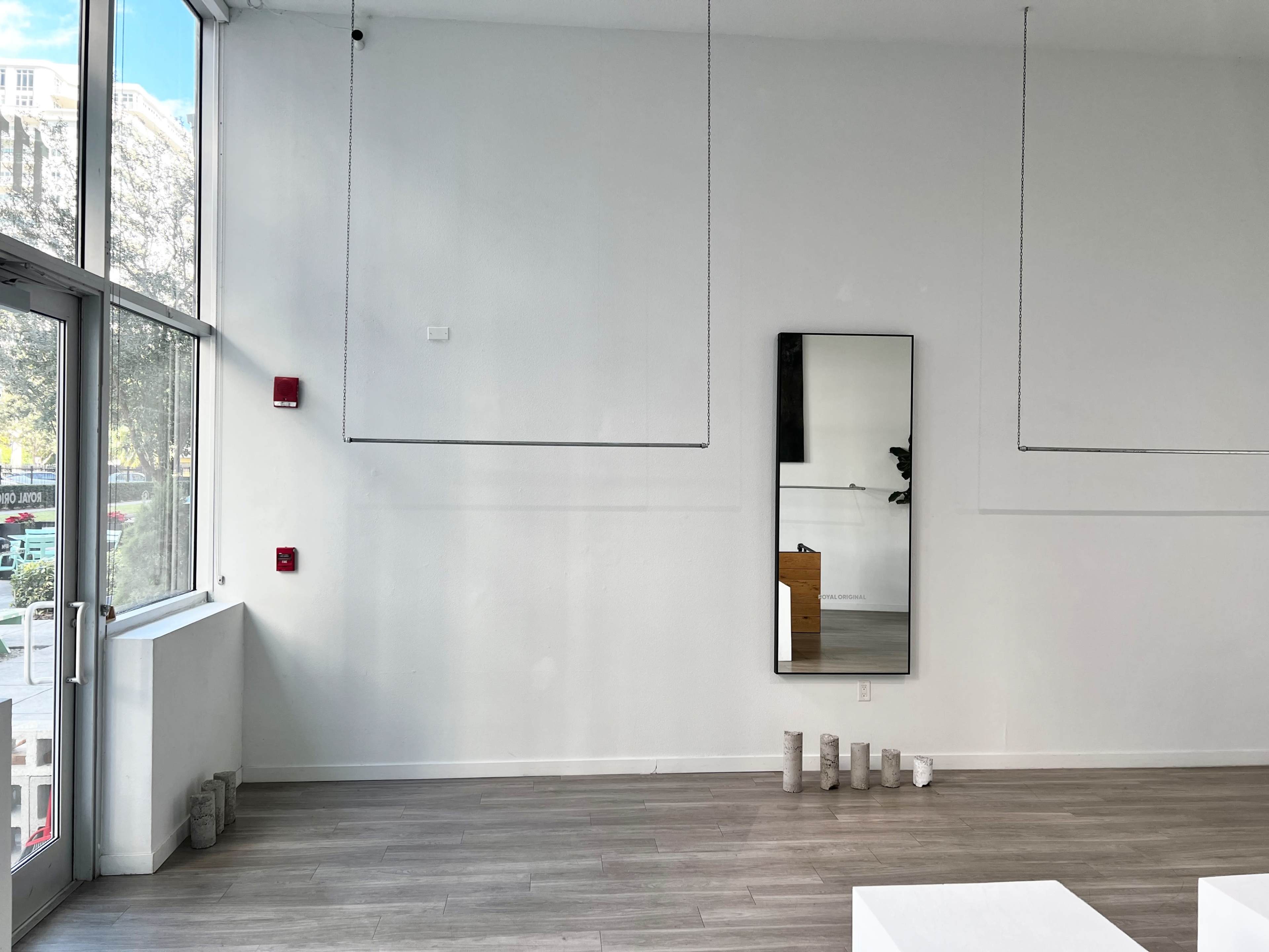 A spacious, empty room features a large mirror on the wall and several cylindrical objects arranged on the floor.