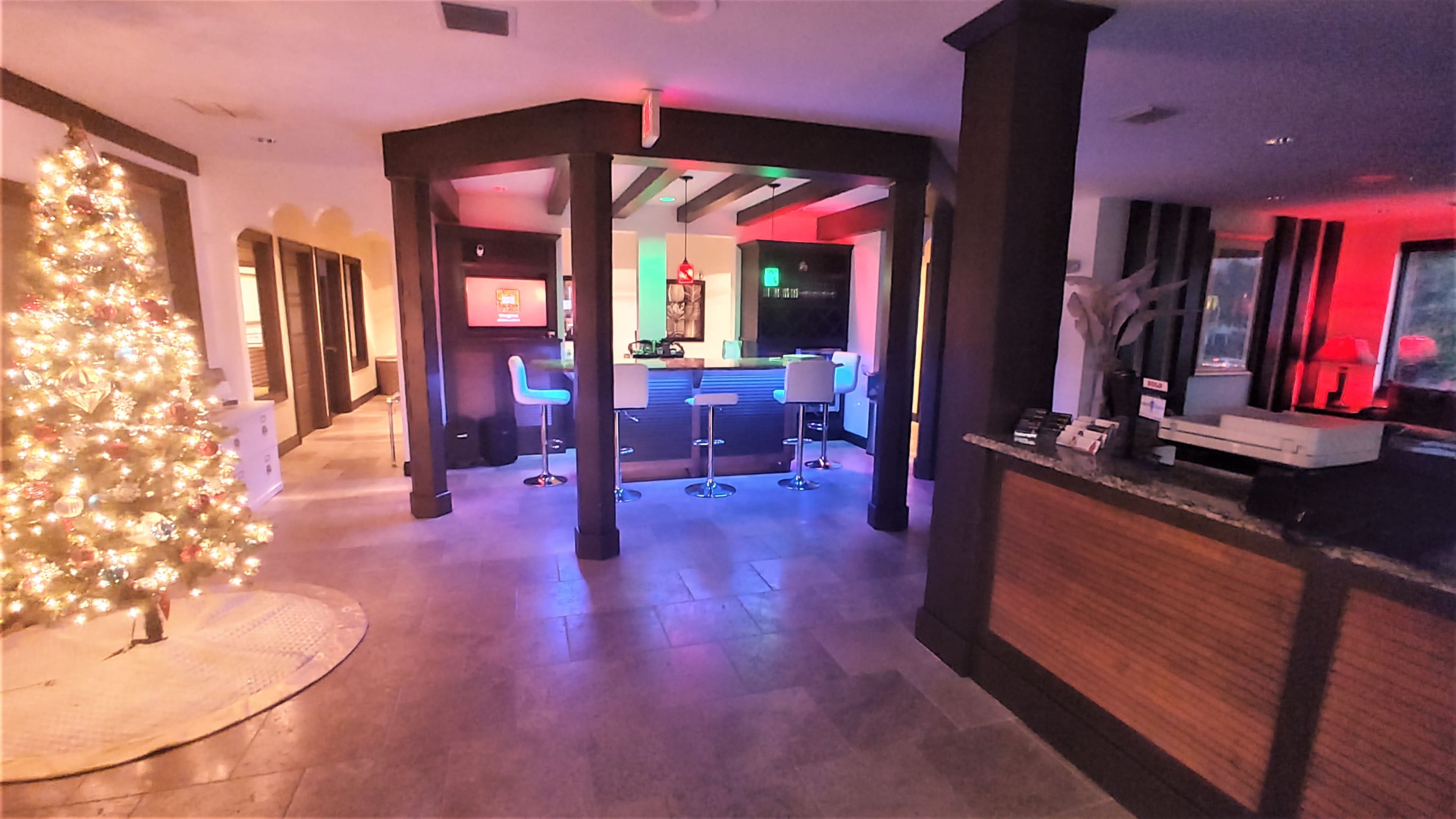A modern reception area with a bar, illuminated by colorful lighting, and a Christmas tree in the corner.