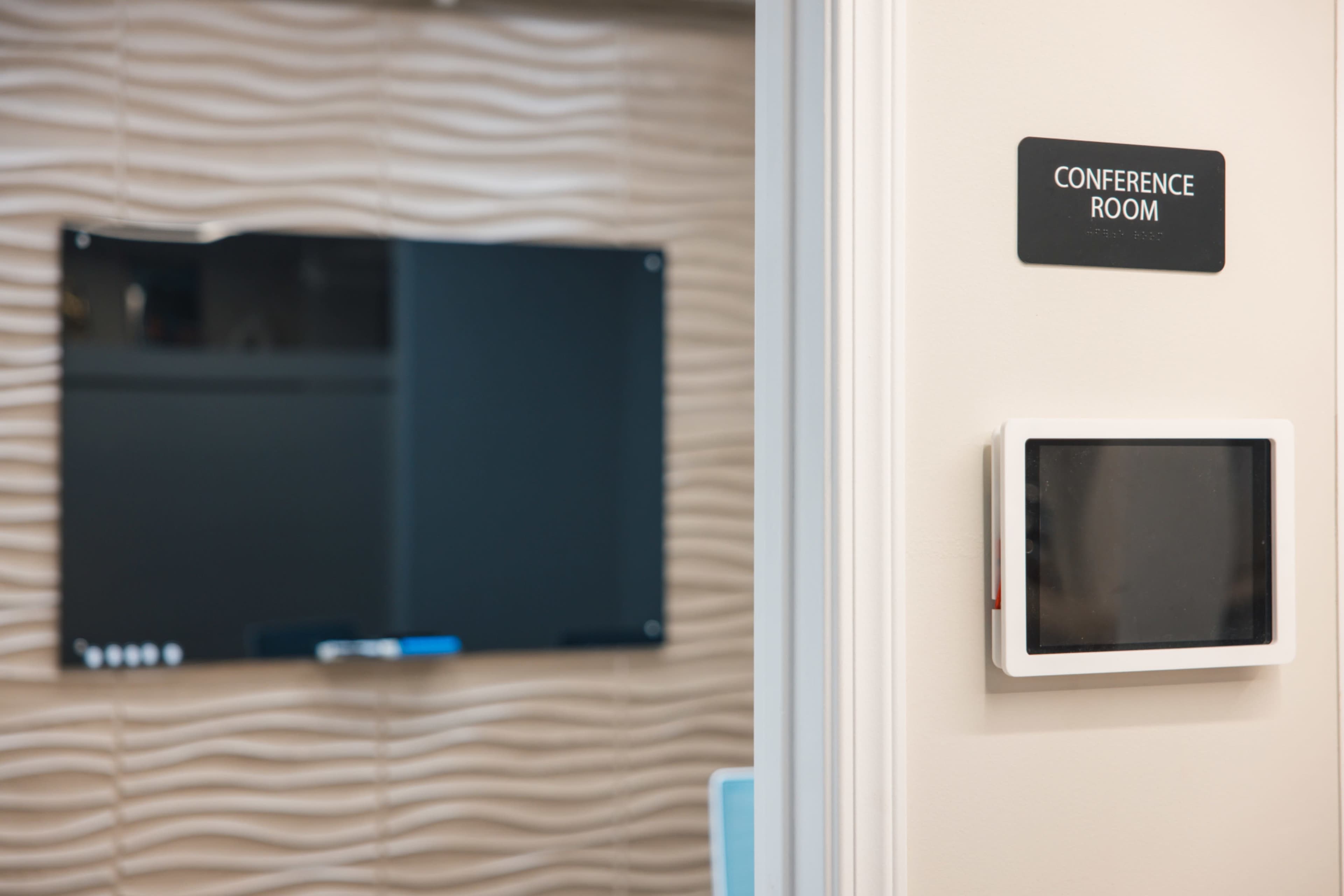 A conference room is identified by a sign mounted on a wall beside a display screen.
