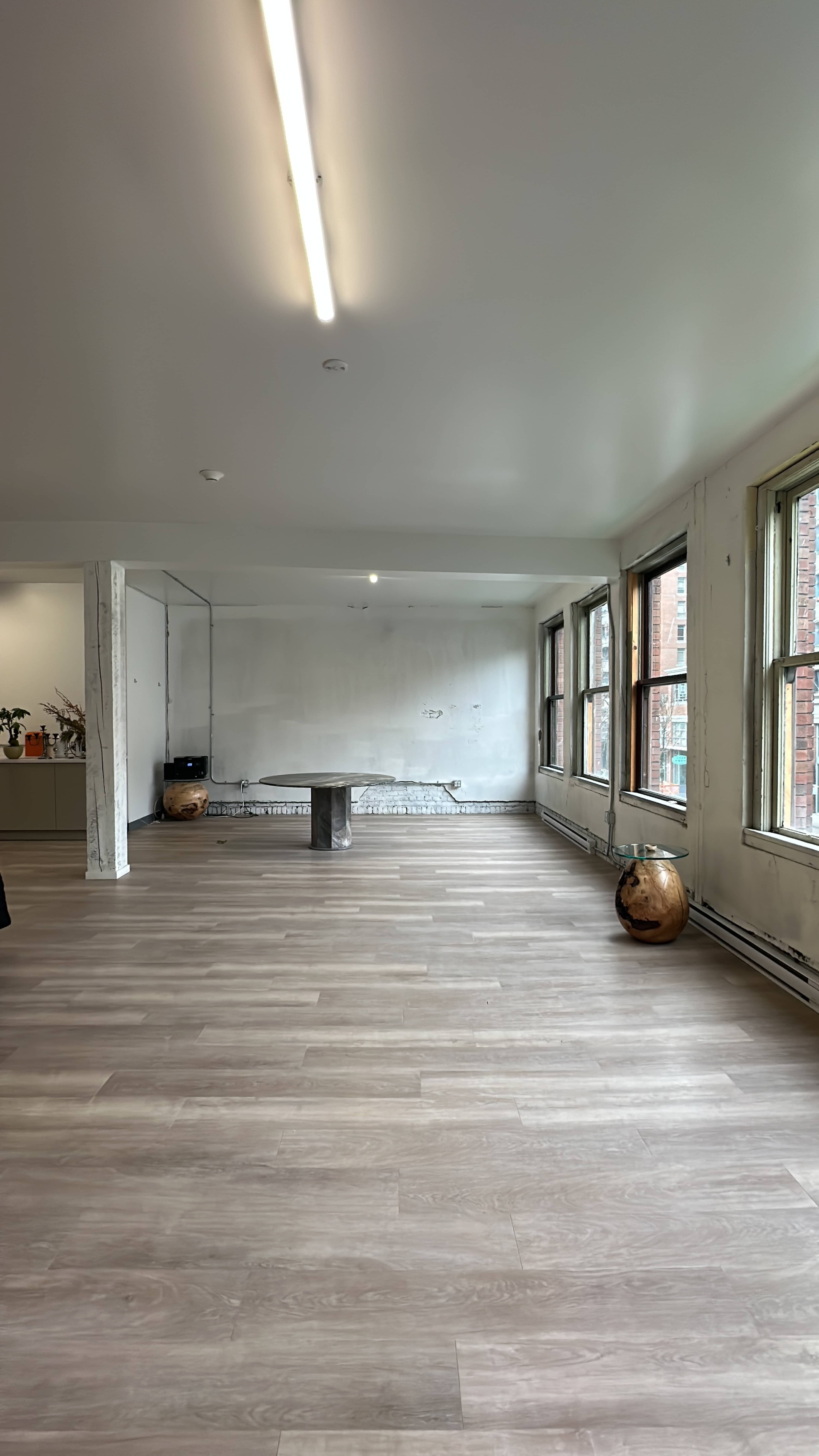 A spacious, empty room with wooden floors, large windows, and a simple table in the center.