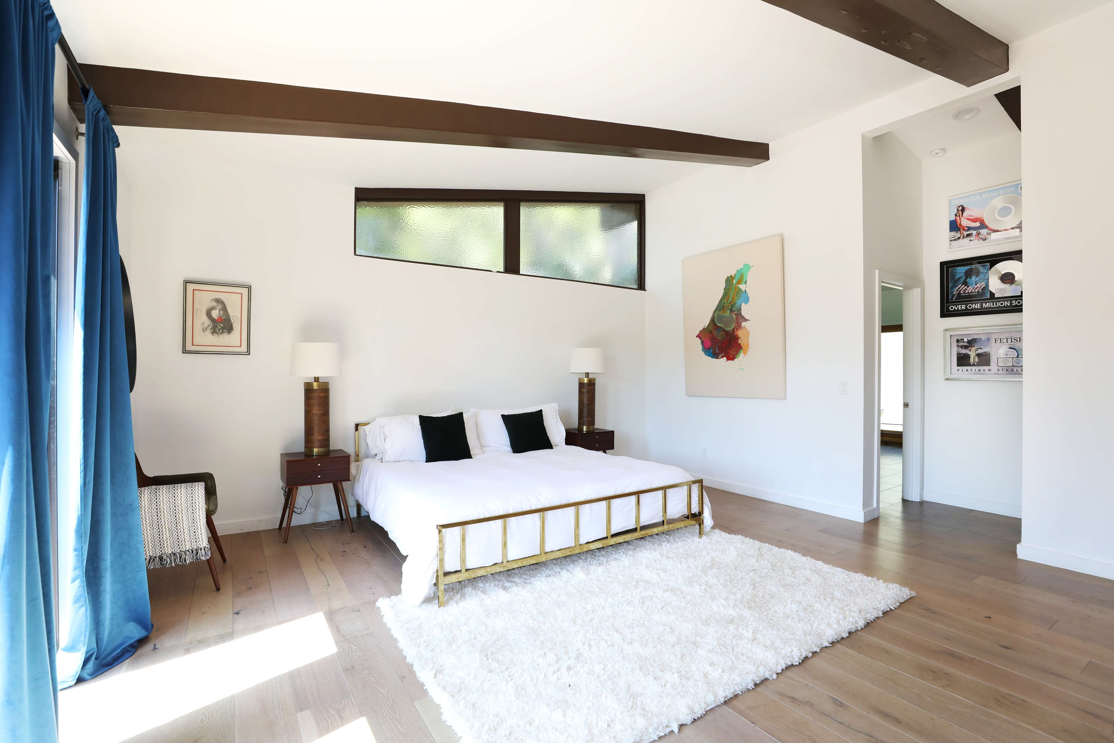 A well-lit bedroom featuring a bed with a white comforter, two bedside tables with lamps, and a large area rug on wooden flooring.