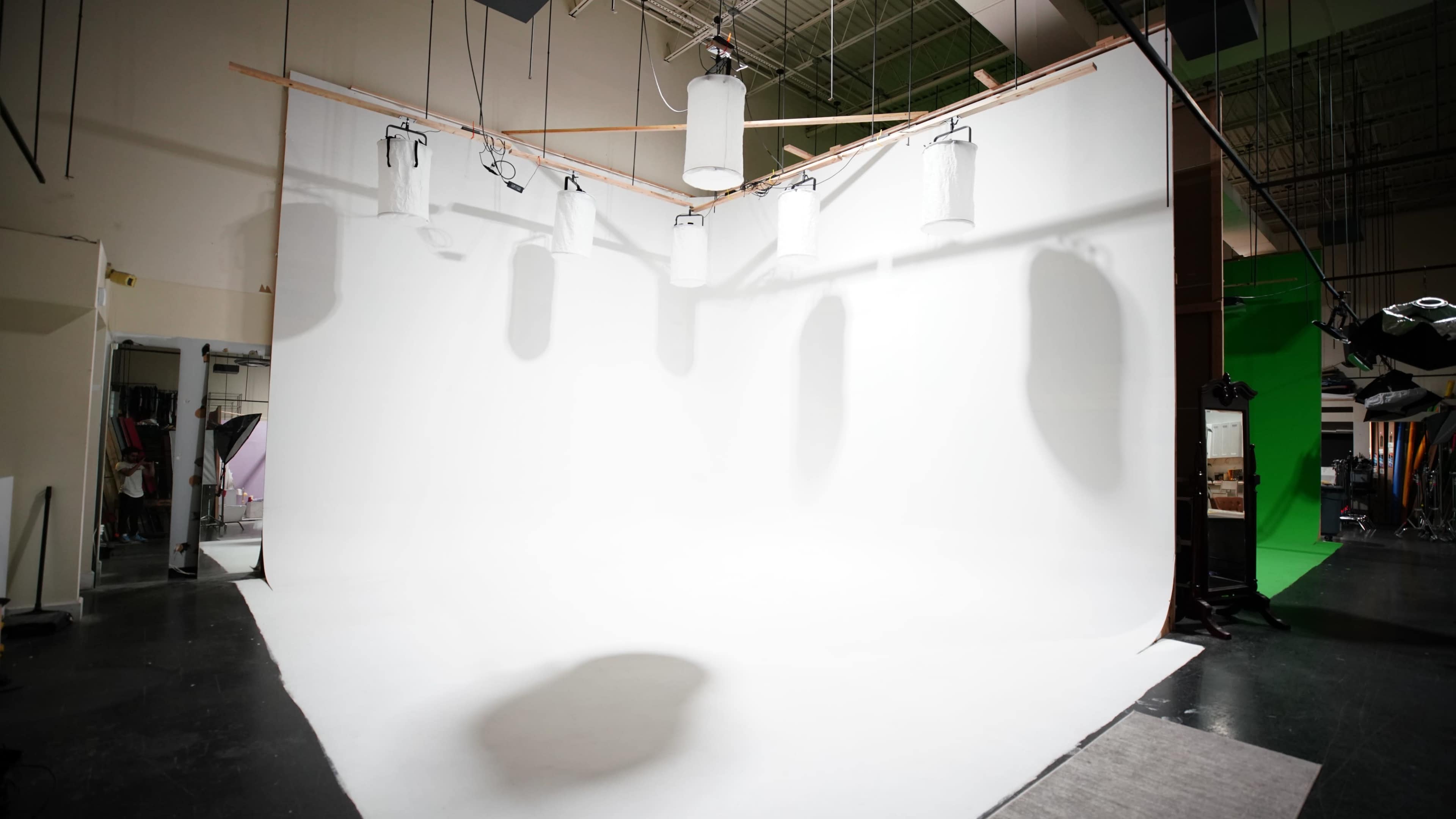 A photography studio with a large white backdrop and multiple hanging light sources.