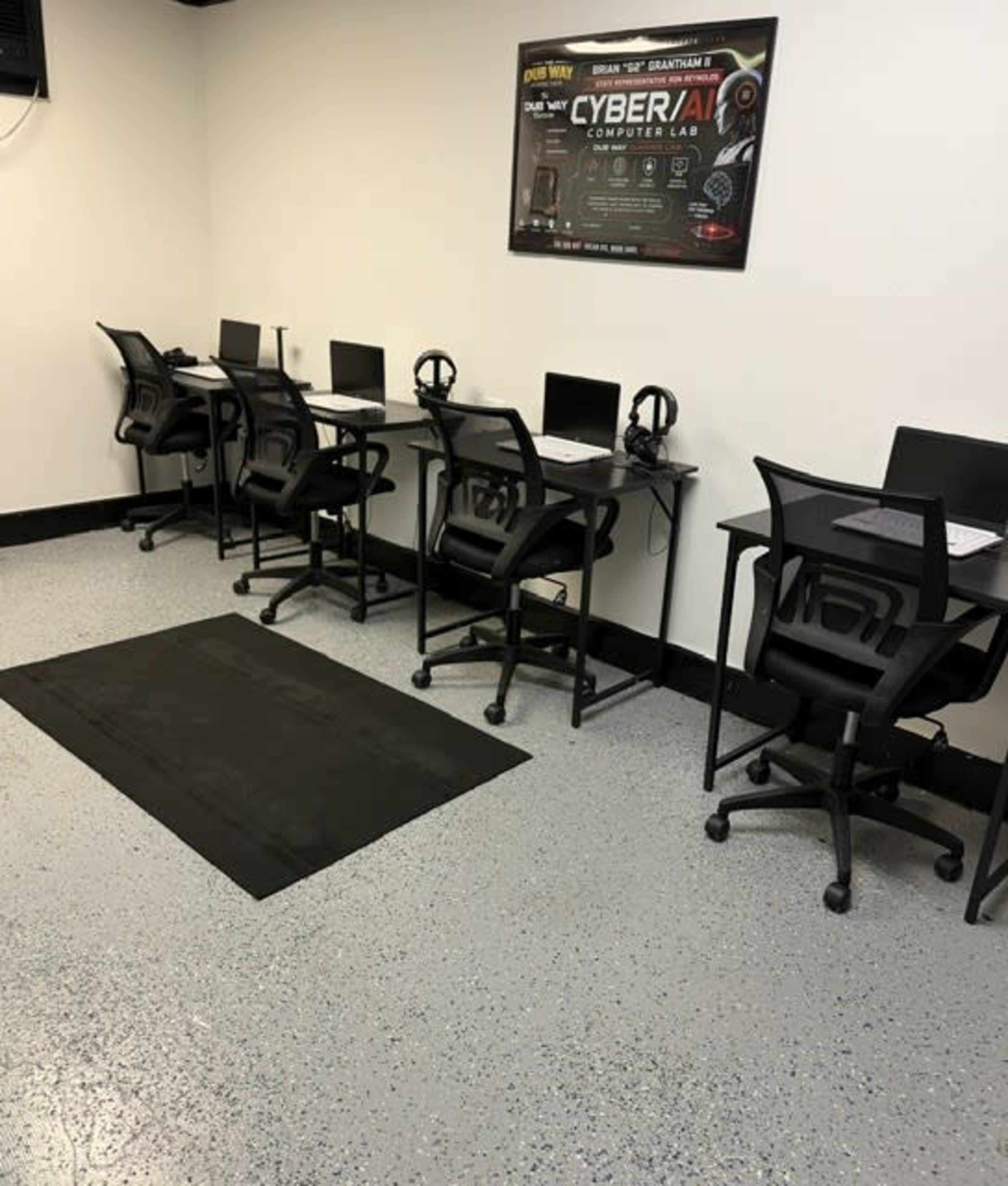 The image shows a computer lab with six workstations, each equipped with a computer and a headset, arranged against a white wall.