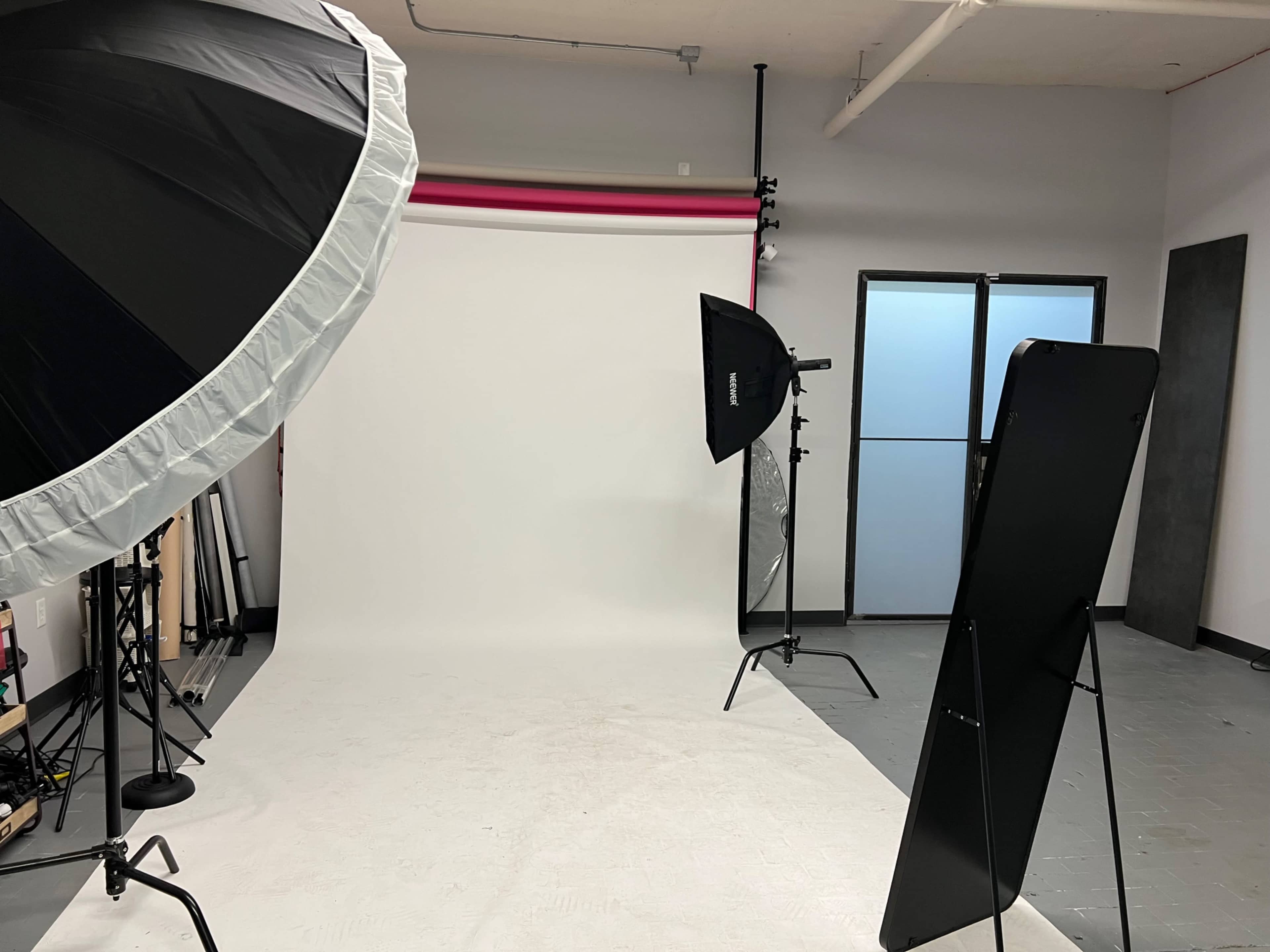 A photography studio with a white backdrop, large softbox lights, and a mirror set up for shoots.