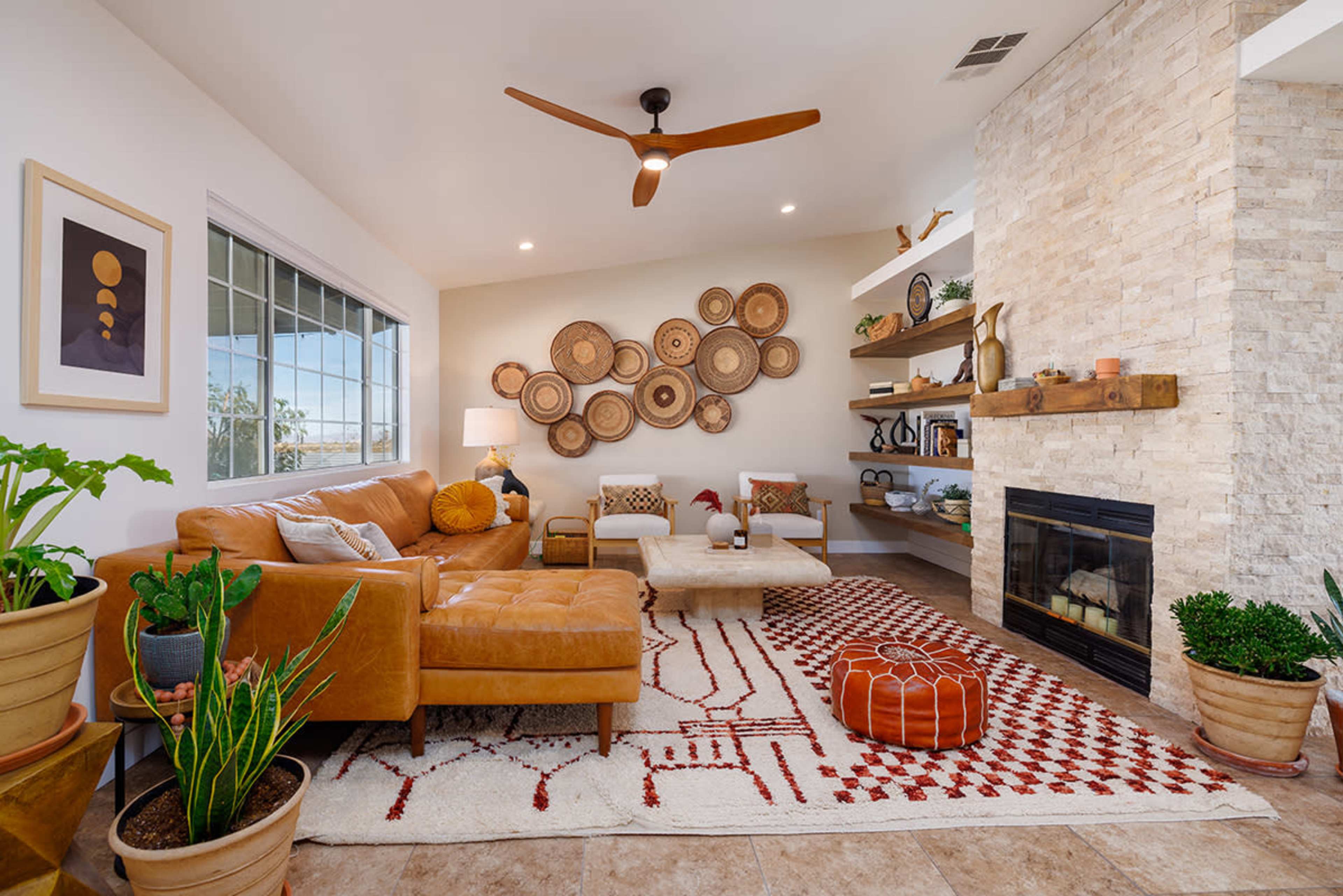 The living room features a tan leather sectional sofa, a round coffee table, and a stone fireplace, with woven art pieces arranged on the wall above.