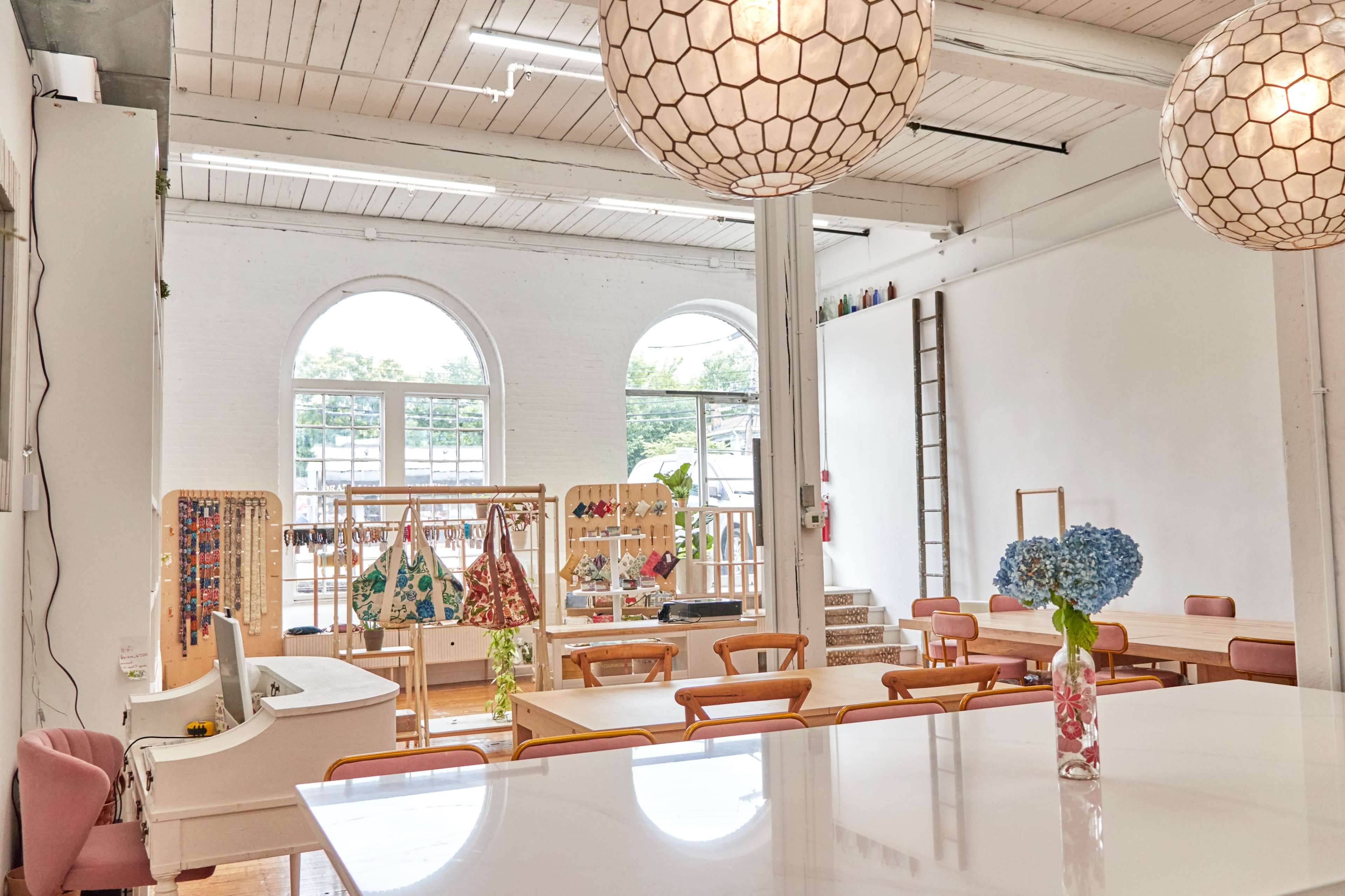 A bright, modern café interior featuring wooden tables, hanging lights, and a display of colorful bags on shelves.