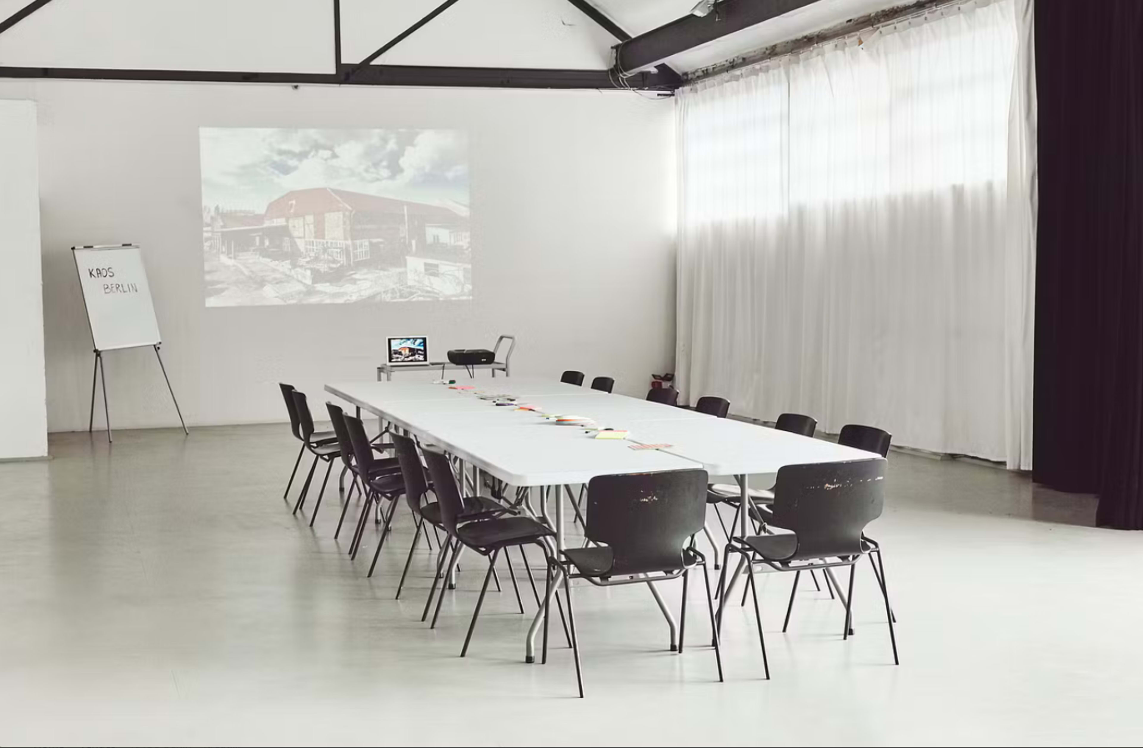 A minimalistic conference room is set up with a long table, black chairs, and a projector displaying an image on the wall.