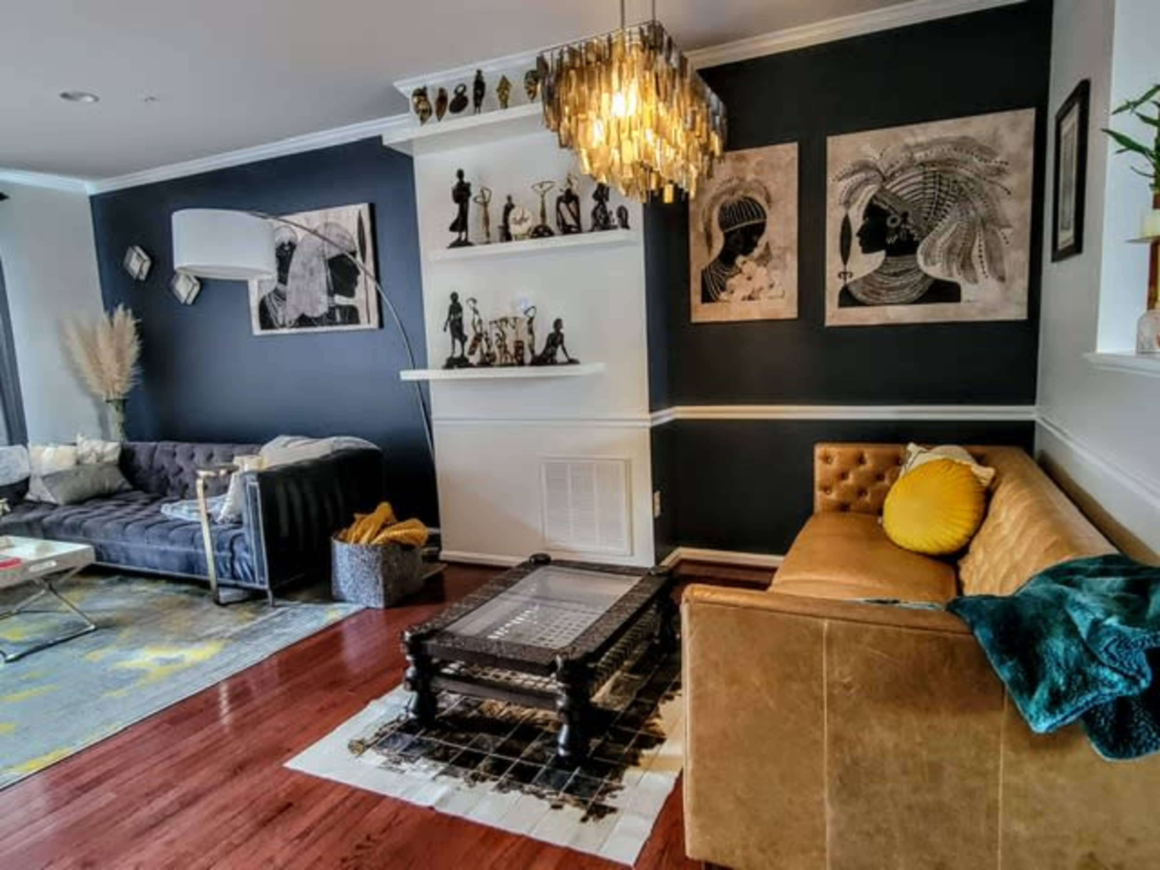 A stylish living room with a mix of dark and light furniture, featuring a brown leather sofa, a gray tufted couch, and two framed artworks on the wall.