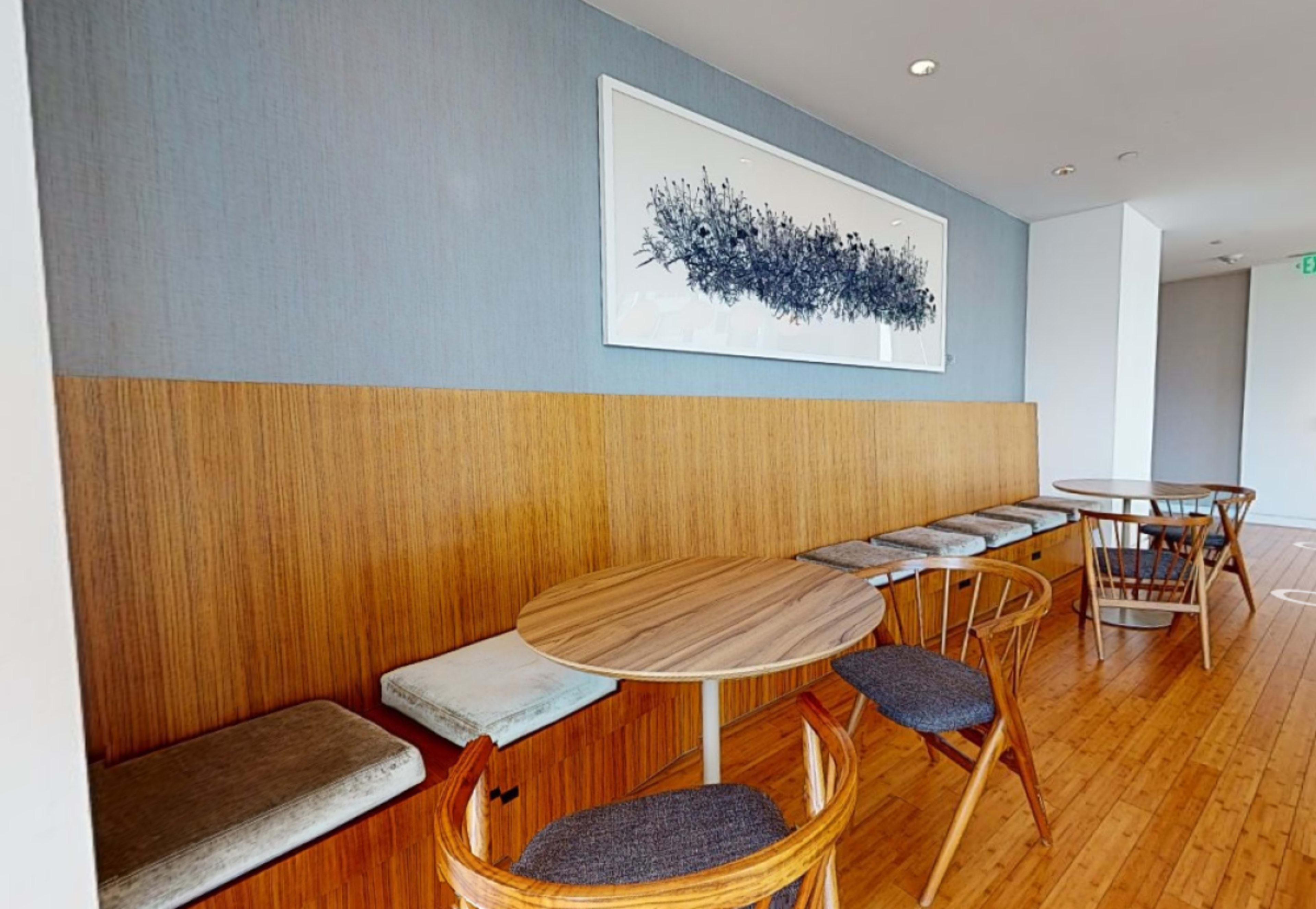 A modern cafe interior features wooden tables and chairs beside a wall adorned with a large framed artwork.