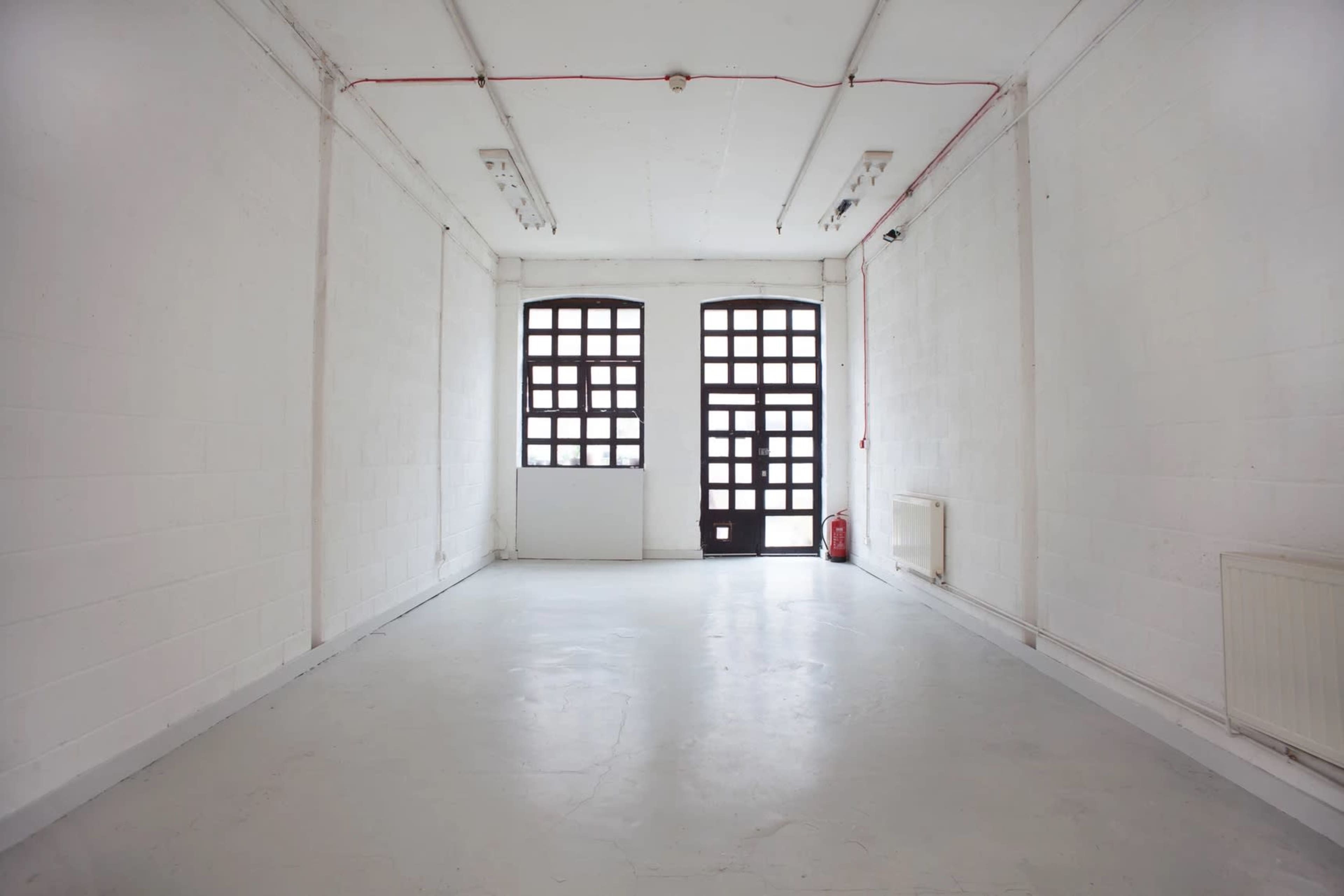 A large, empty room with white walls, a concrete floor, and two large windows on one side.