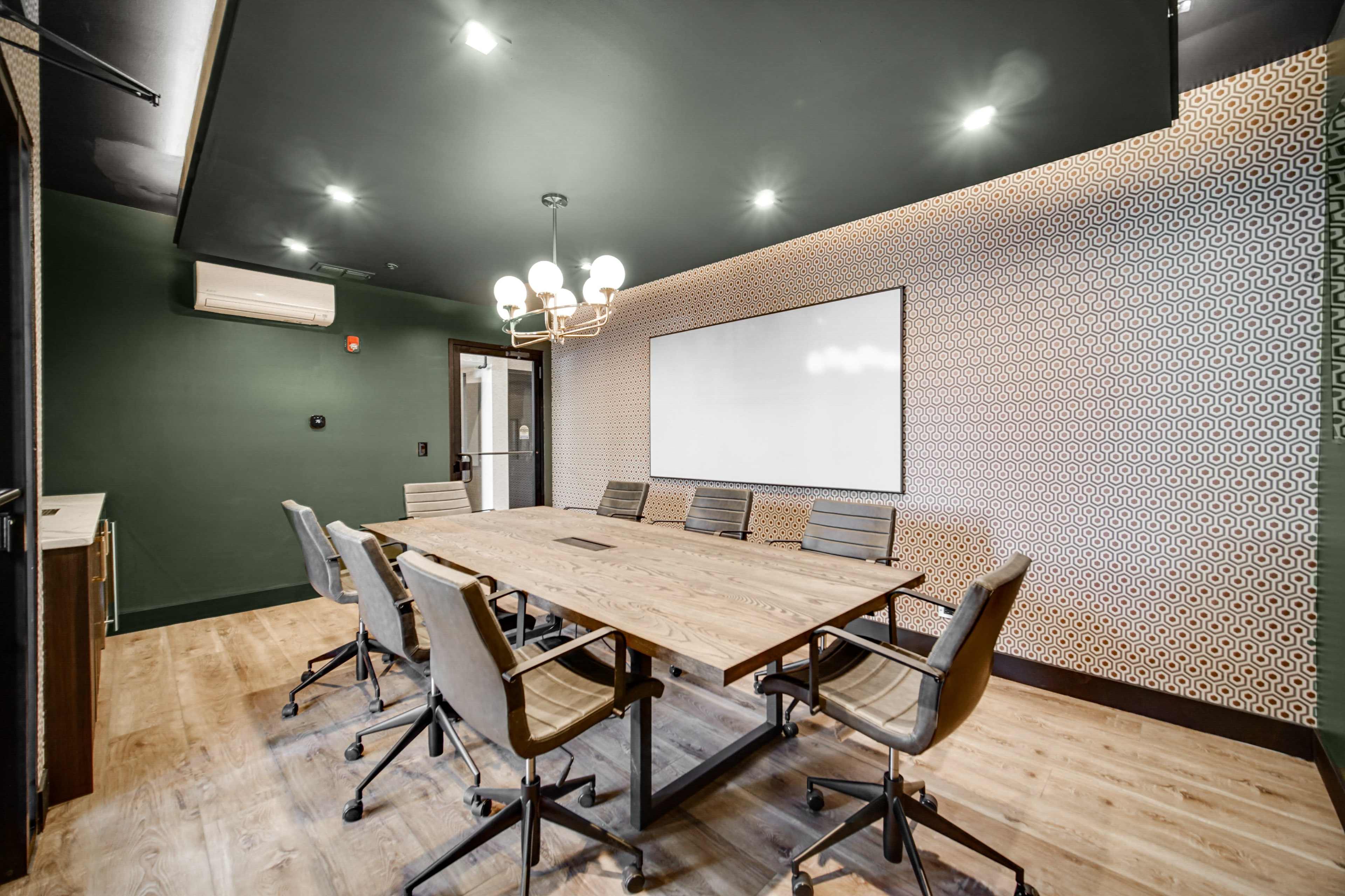 A modern conference room features a large wooden table surrounded by ergonomic chairs, with an accent wall of geometric patterns and a whiteboard at the front.
