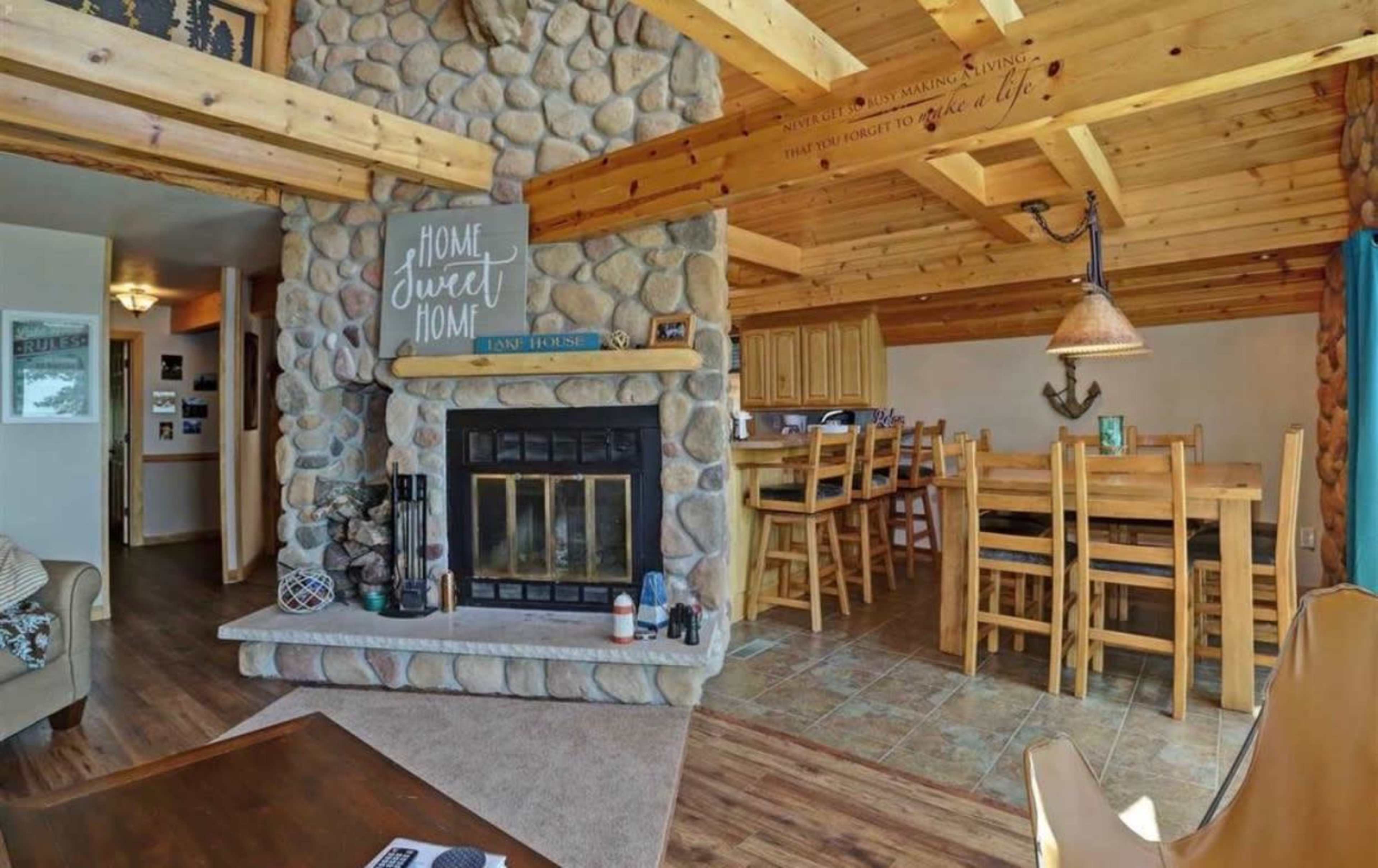 A cozy living space with a stone fireplace, wooden ceiling beams, and a dining area featuring a wooden table and chairs.