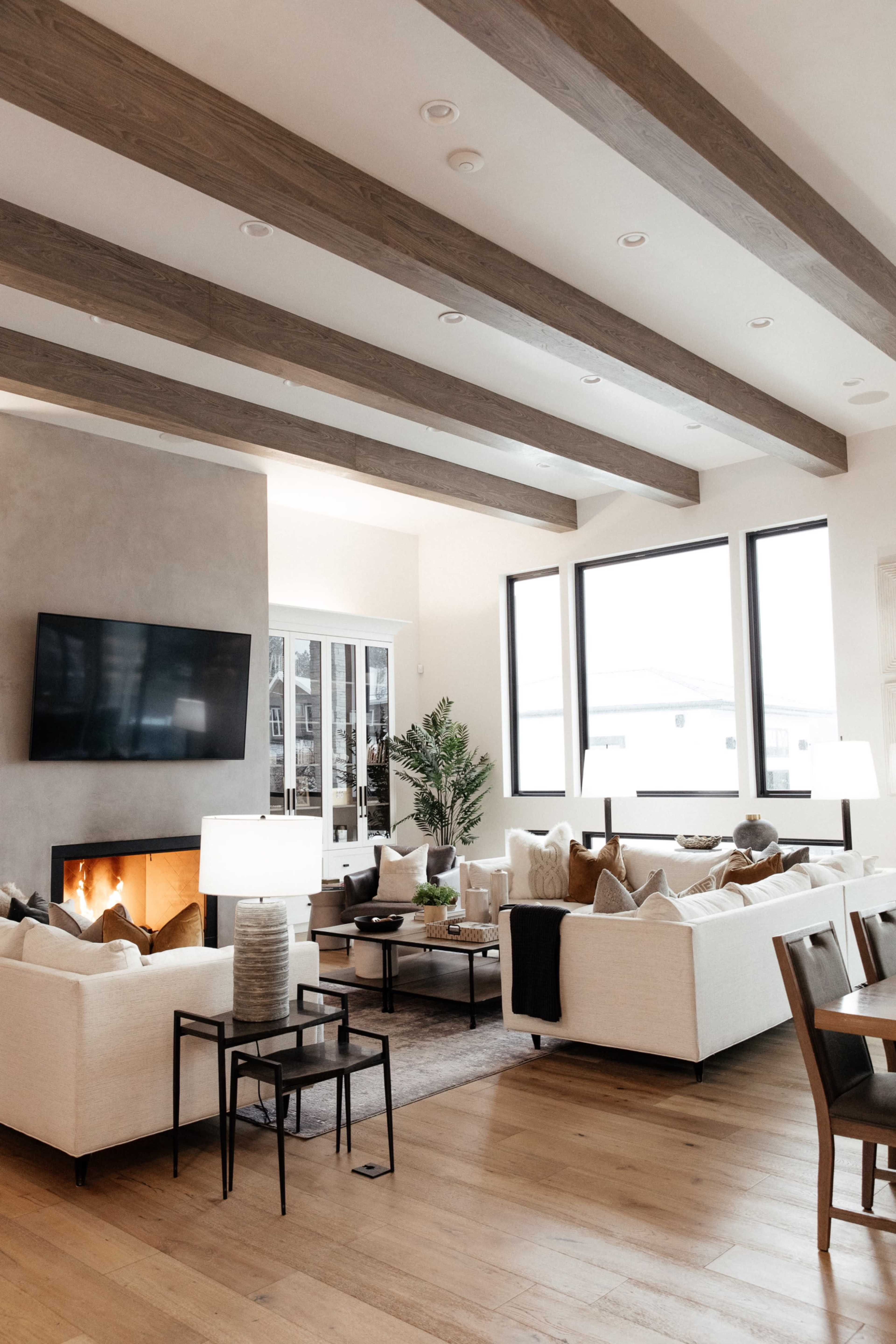 A modern living room with white sectional sofas, a fireplace, and large windows providing natural light.