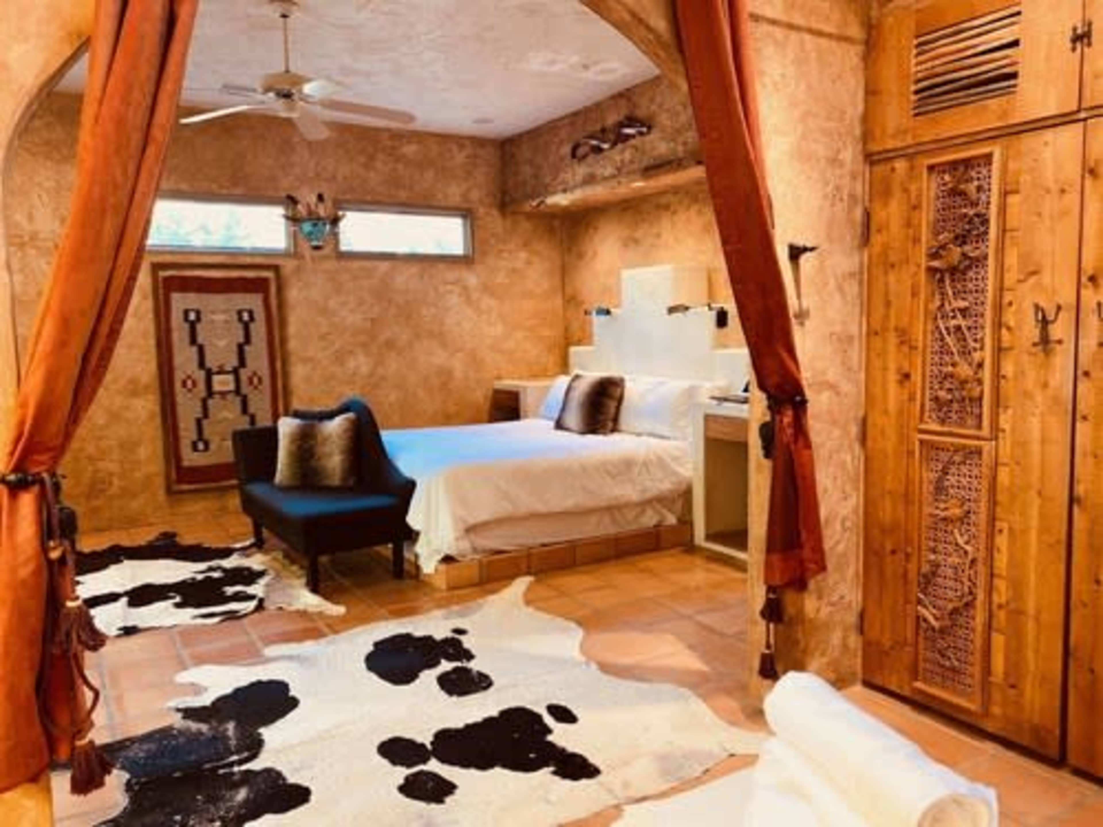 A bedroom with a bed, a seating area, and cowhide rugs on the tiled floor.