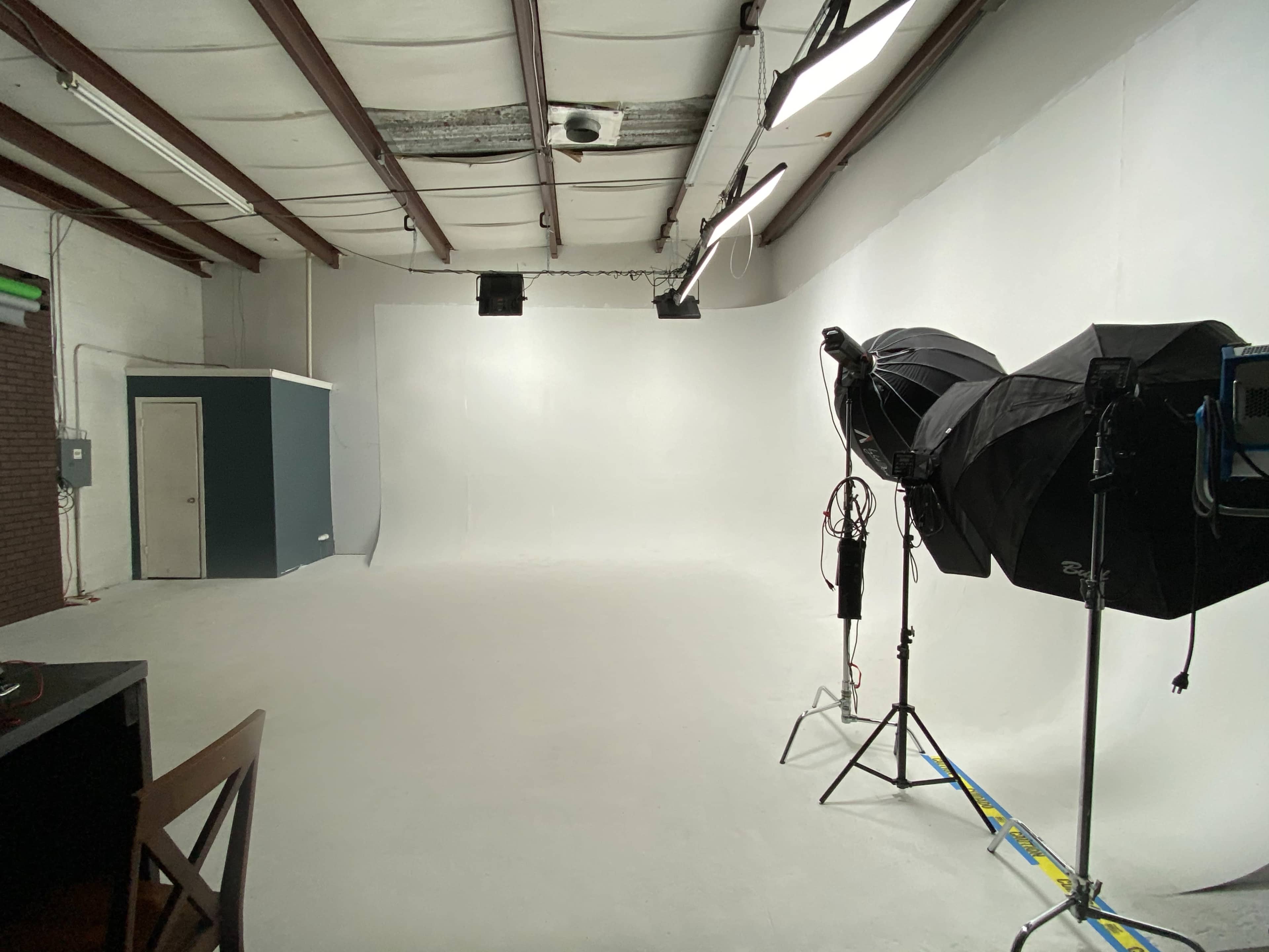 A spacious photography studio with a white backdrop, softbox lighting, and a door to the side.