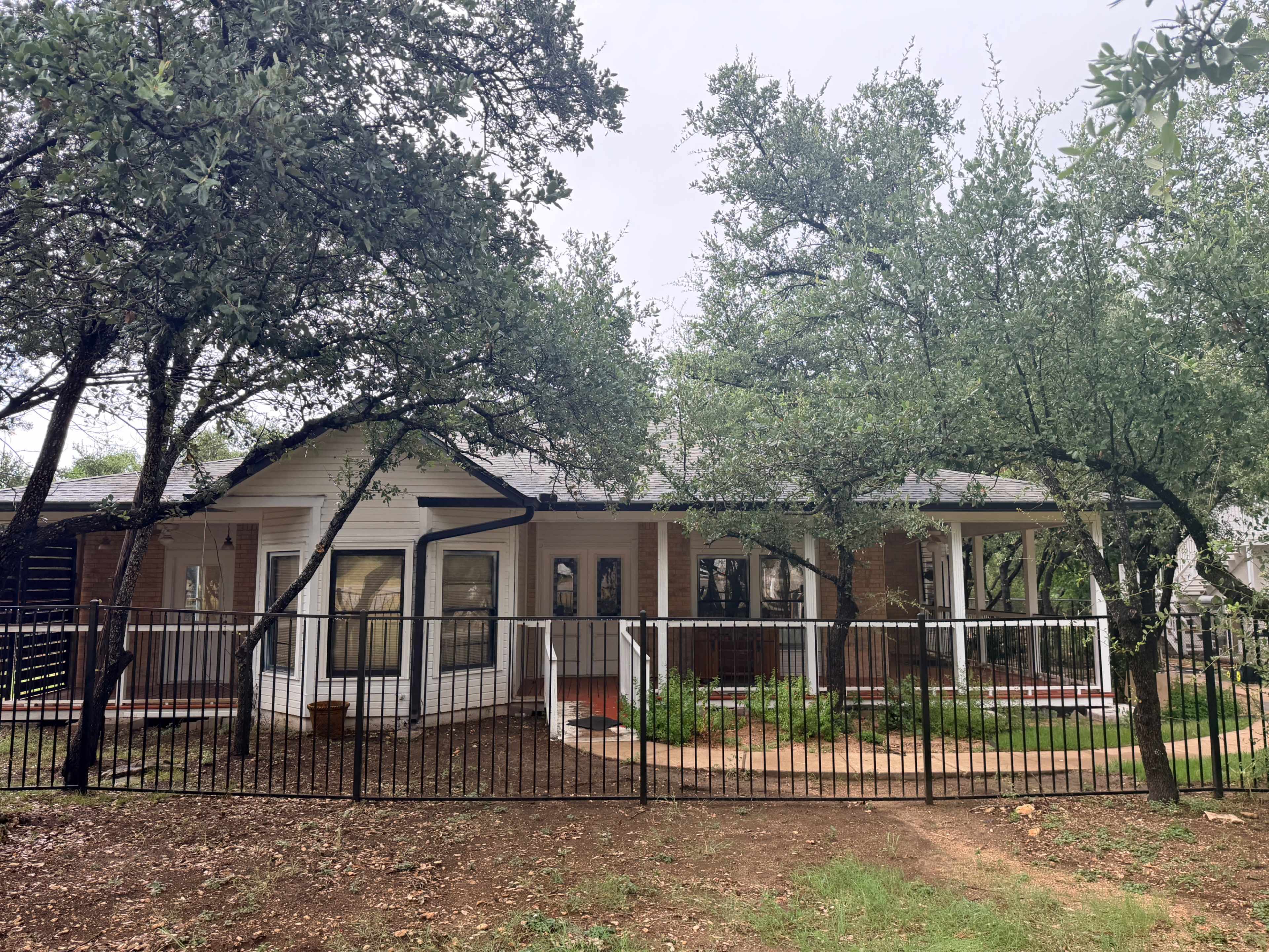 A single-story house with a fenced yard, surrounded by several trees and shrubs.